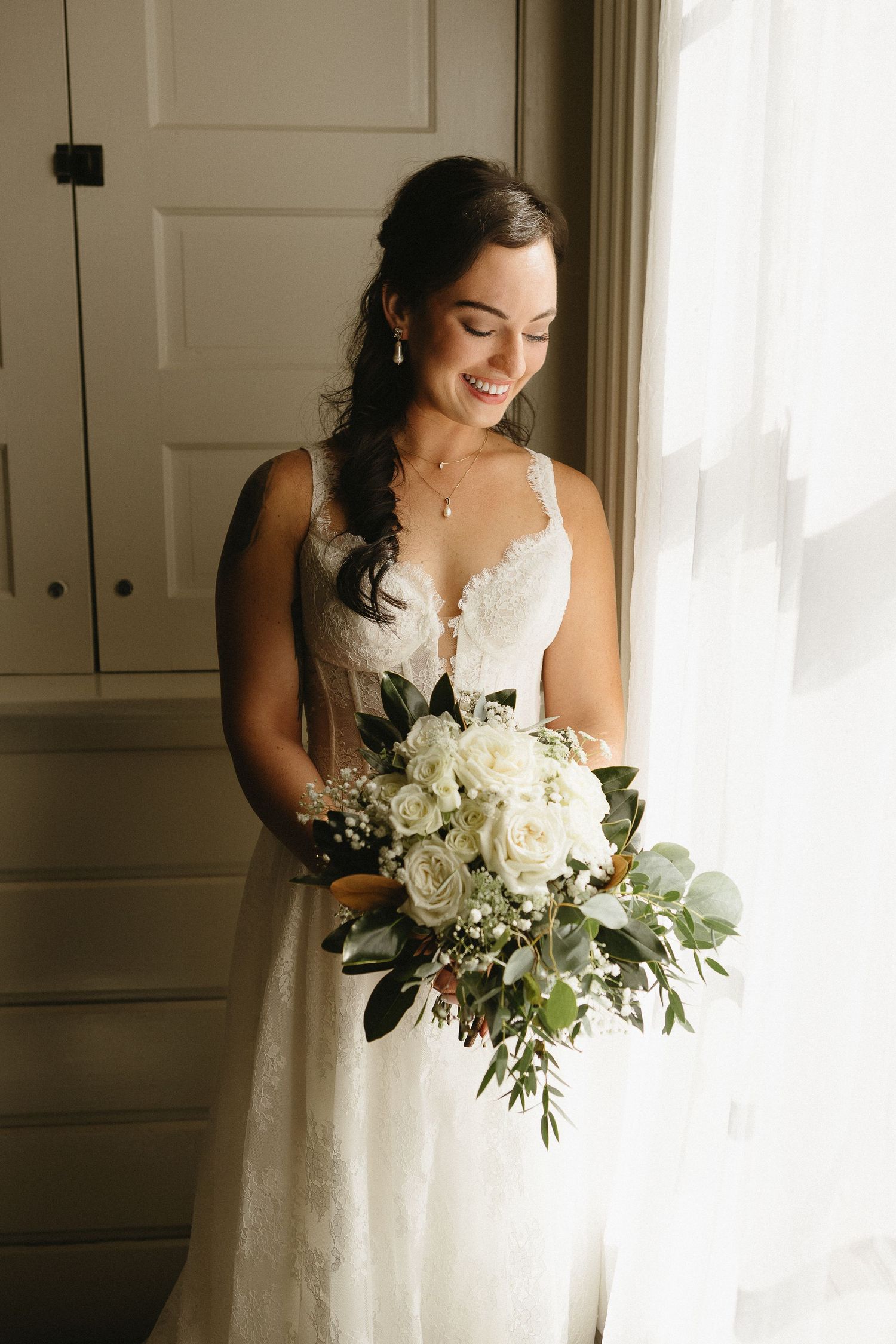 Elegant bridal bouquet featuring white roses and greenery in natural window light.