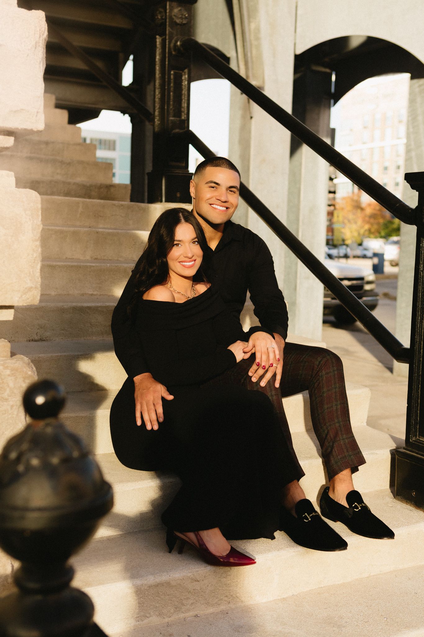 A happy couple sitting together on marble steps with classic architectural details in warm lighting.