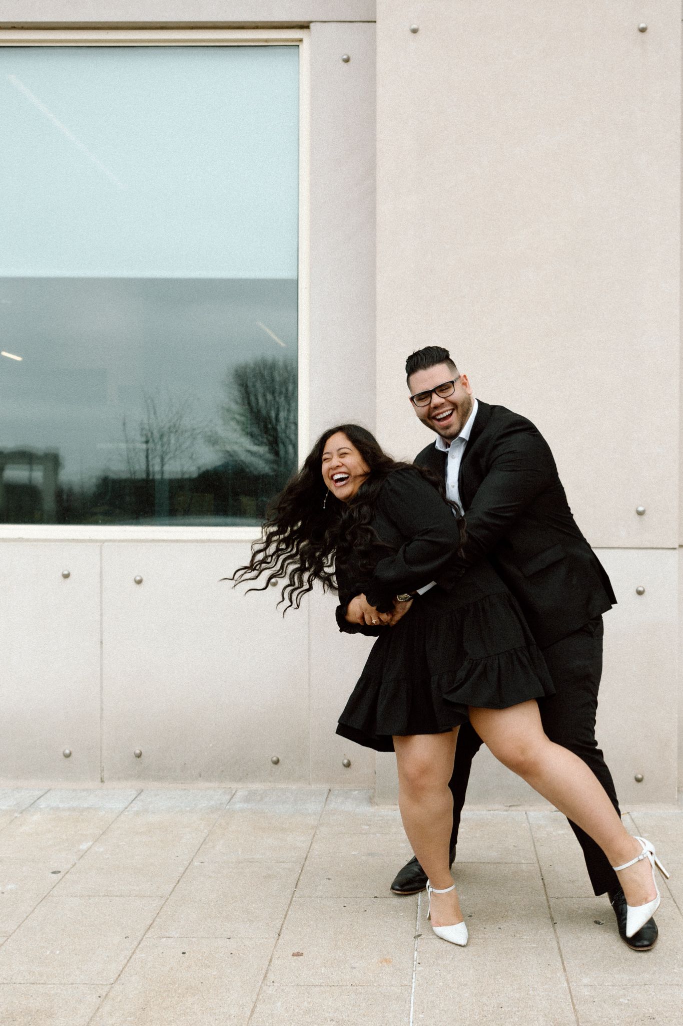 Engaged couple in downtown Louisville, with the woman smiling and showing her engagement ring while embracing her fiancé