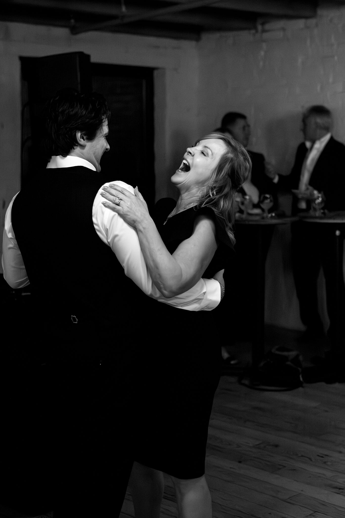 A joyful couple laughing while dancing together at a wedding reception in black and white photography.