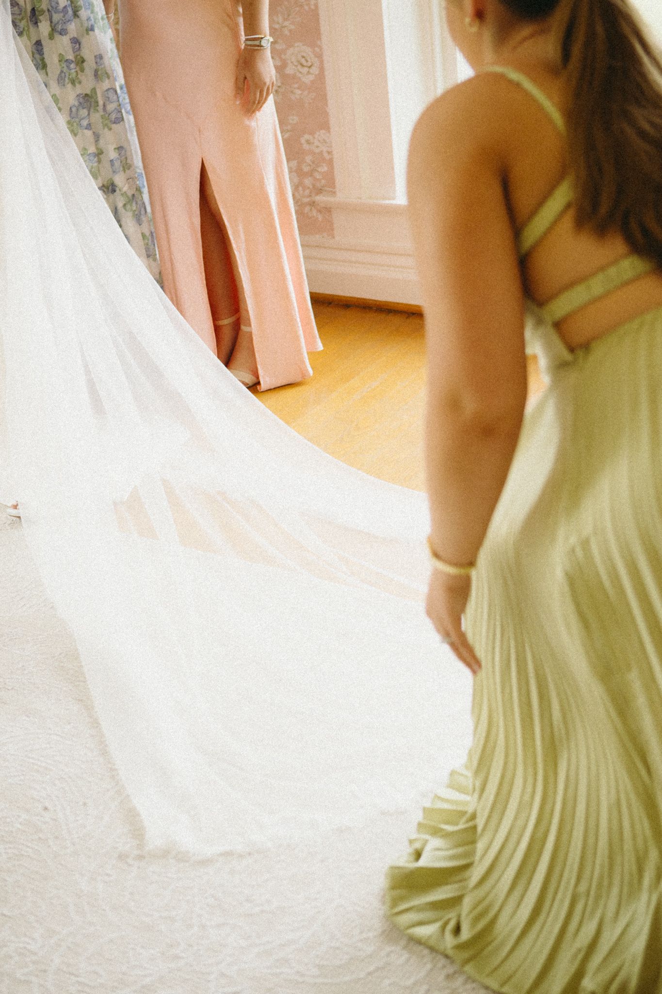 Bridesmaids in pale yellow dresses help arrange a flowing white wedding veil.