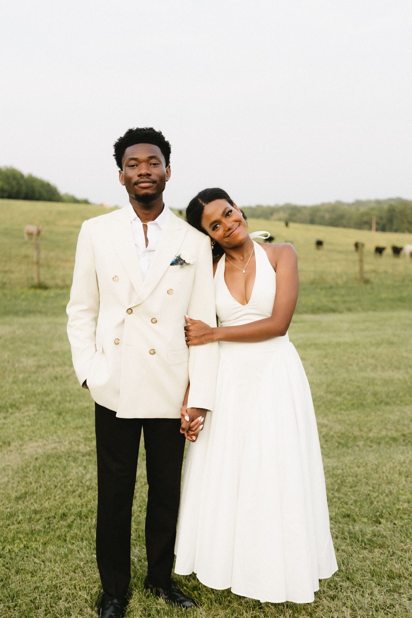 Wedding couple poses together in green field wearing elegant white attire.