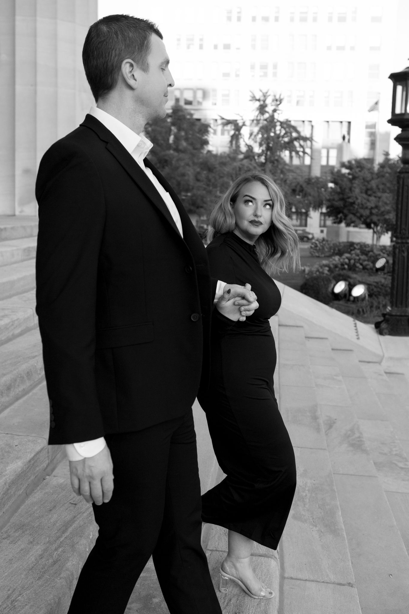 A couple in formal wear stands together in black and white against a columned backdrop.