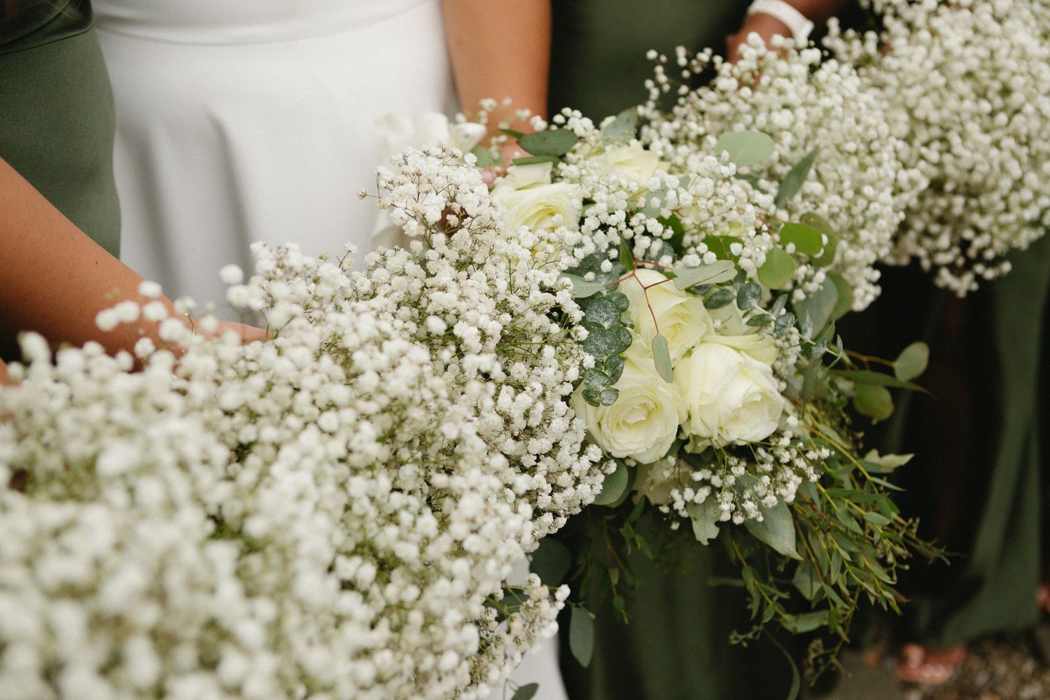 Beautiful white baby's breath and rose bouquet held against a dark green background.