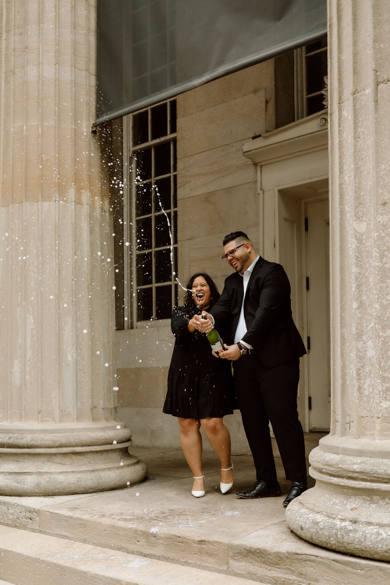 Engaged couple celebrating with a bottle of Chandon, sharing a joyful moment and laughter in downtown Louisville
