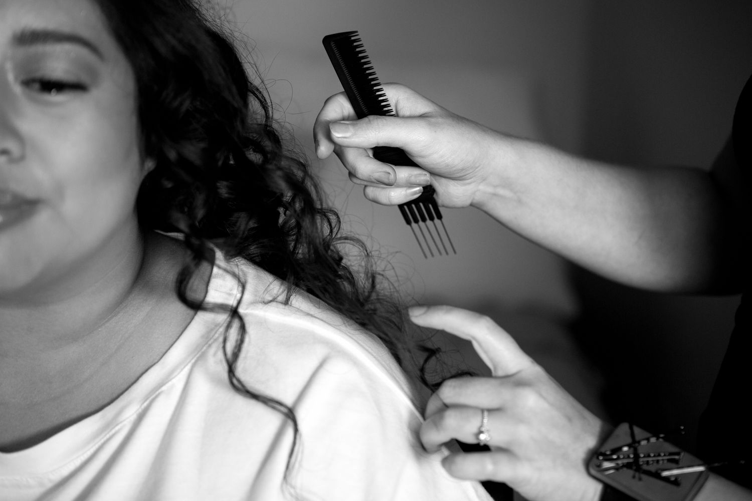 A hairstylist holds a comb and styling tools while working on curly hair in black and white photography.