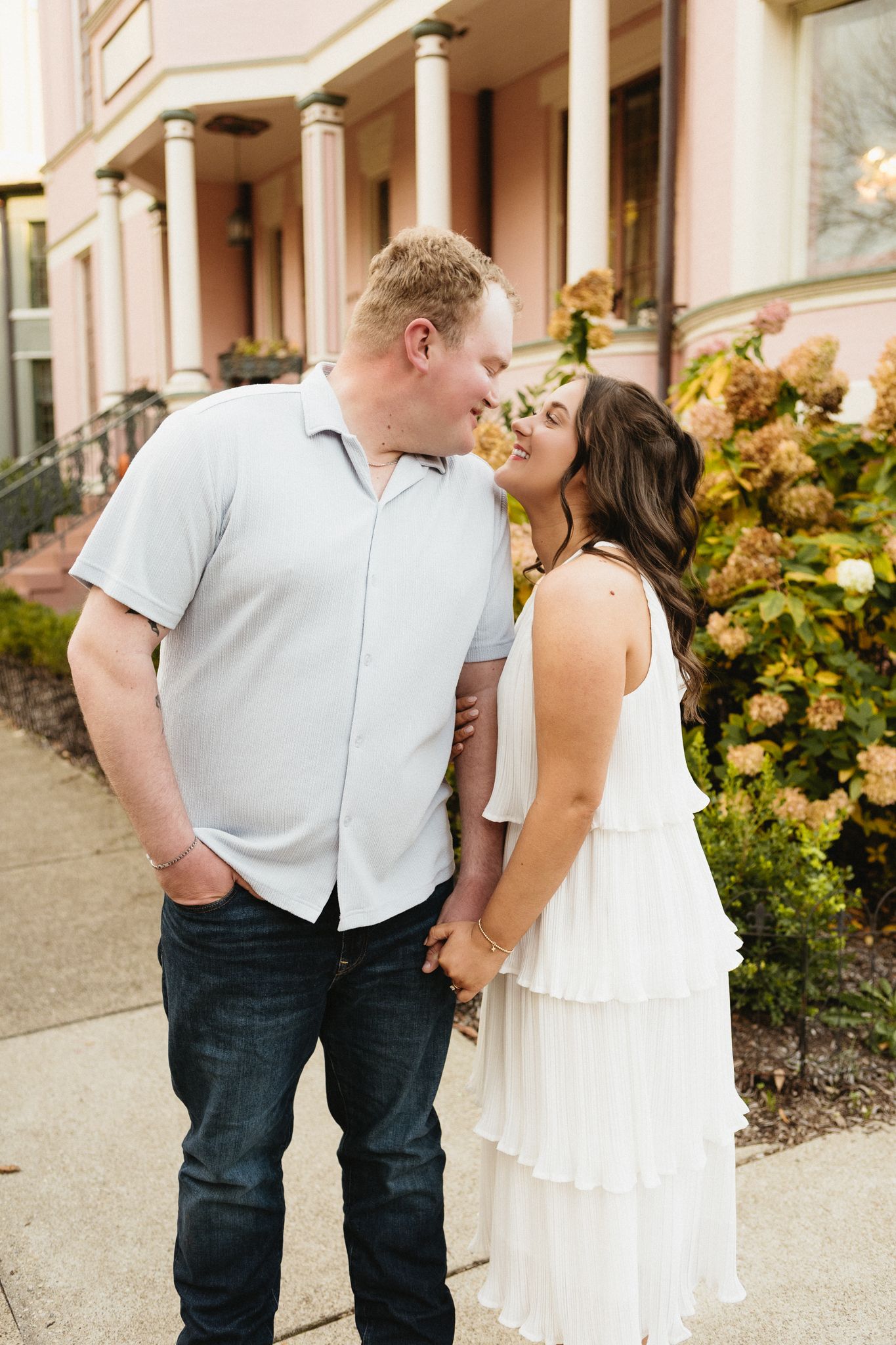 A tender moment shared between a couple in front of a pink building with classical columns.