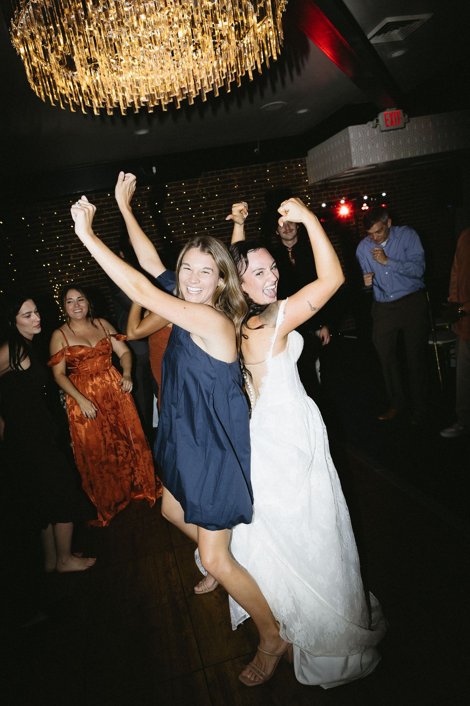 Wedding reception dance party under crystal chandeliers with guests celebrating.
