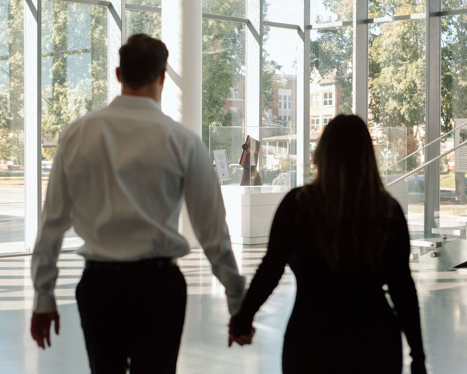 Engaged couple in downtown Louisville, with the woman smiling and showing her engagement ring while embracing her fiancé