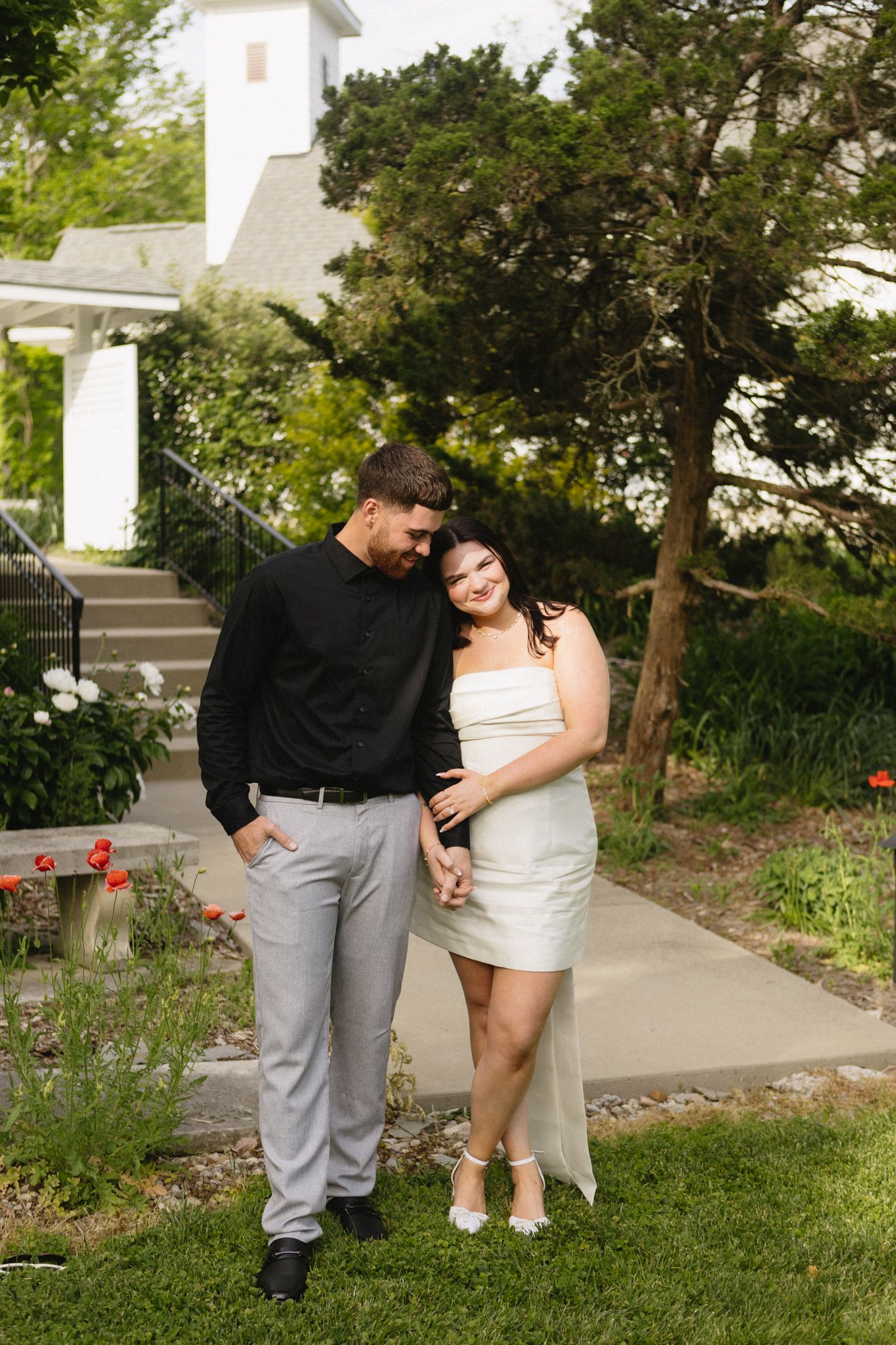 Couple sharing tender moments together in a garden setting with trees and greenery in the background.
