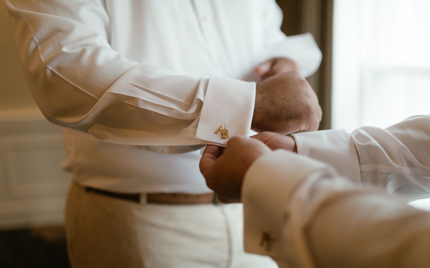 Close-up view of person adjusting white dress shirt cuffs and silver cufflinks before formal event.