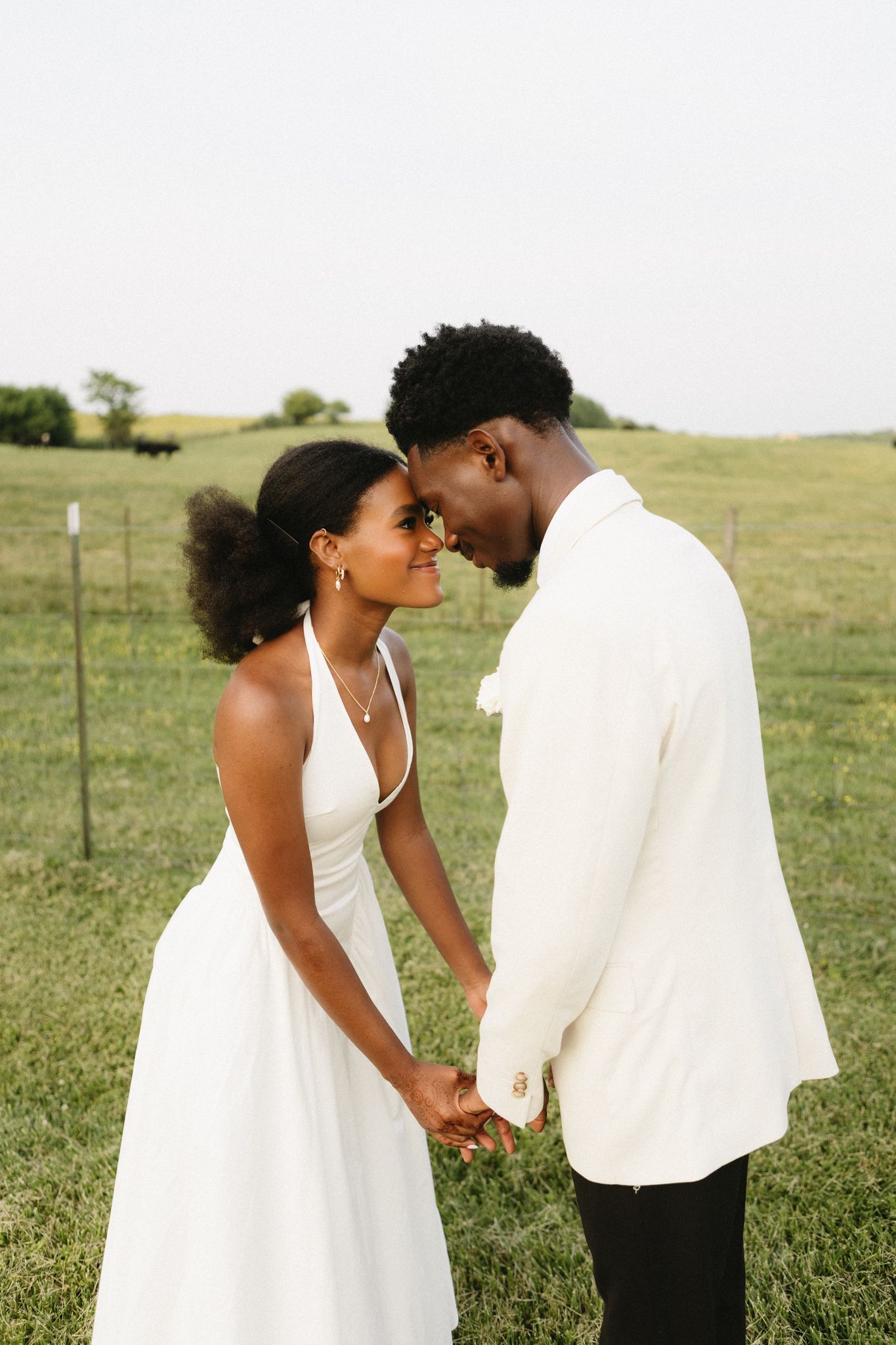 A romantic wedding couple shares an intimate moment in a grassy field while wearing elegant white attire.