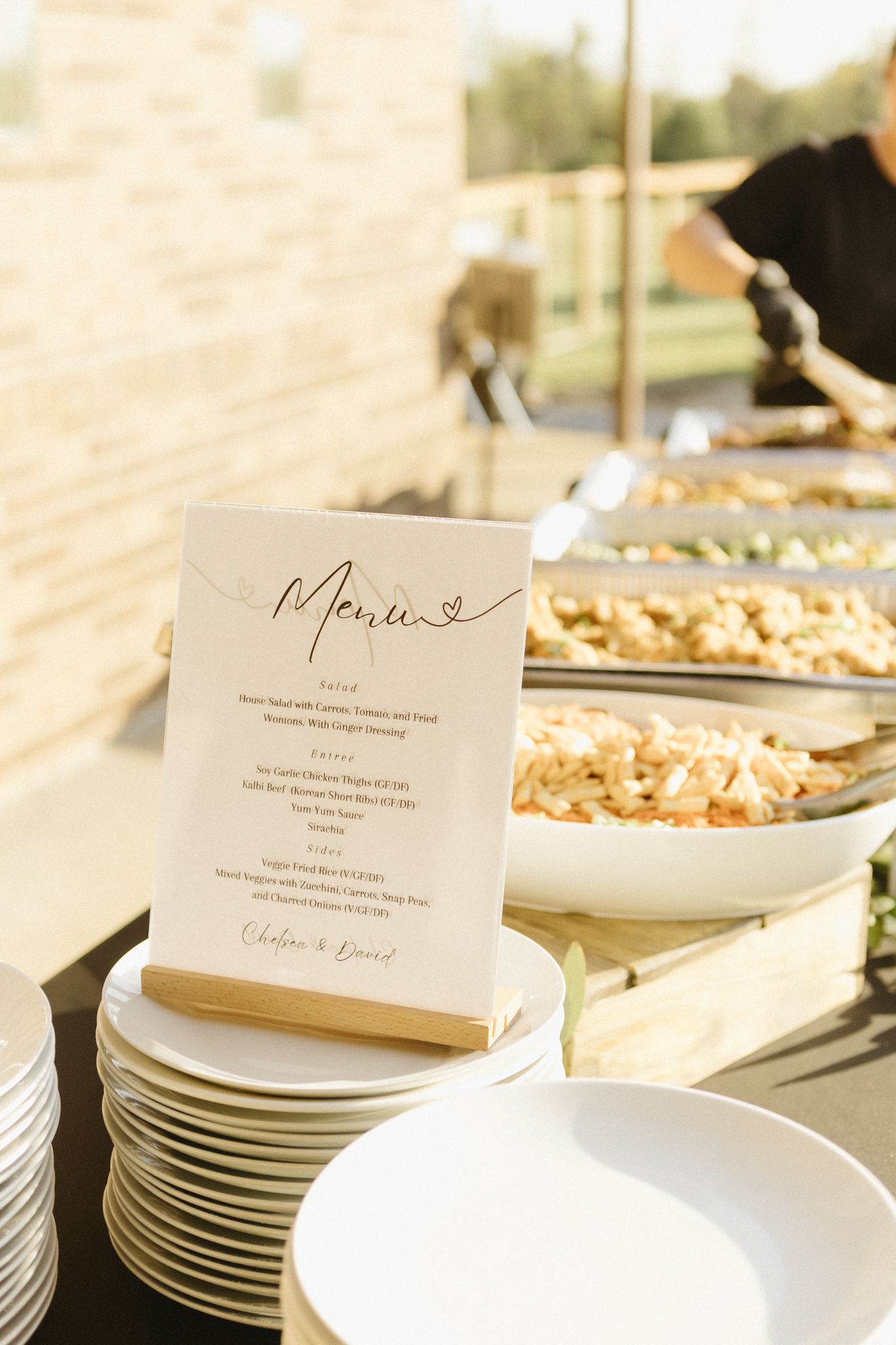 White plates stacked neatly on a buffet table with elegant menu cards displayed.