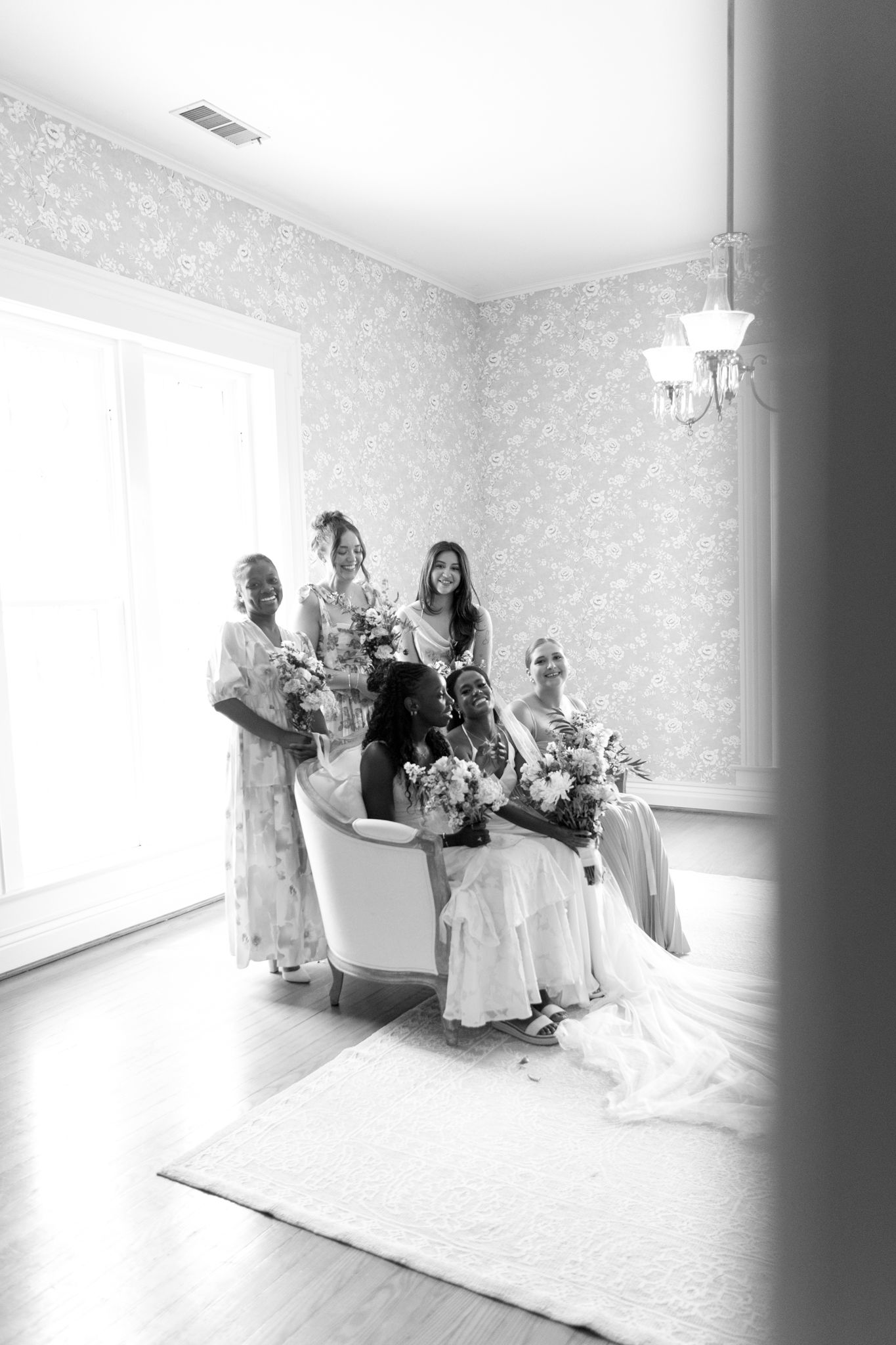 Bridal party in light airy room with white floral wallpaper and natural lighting.