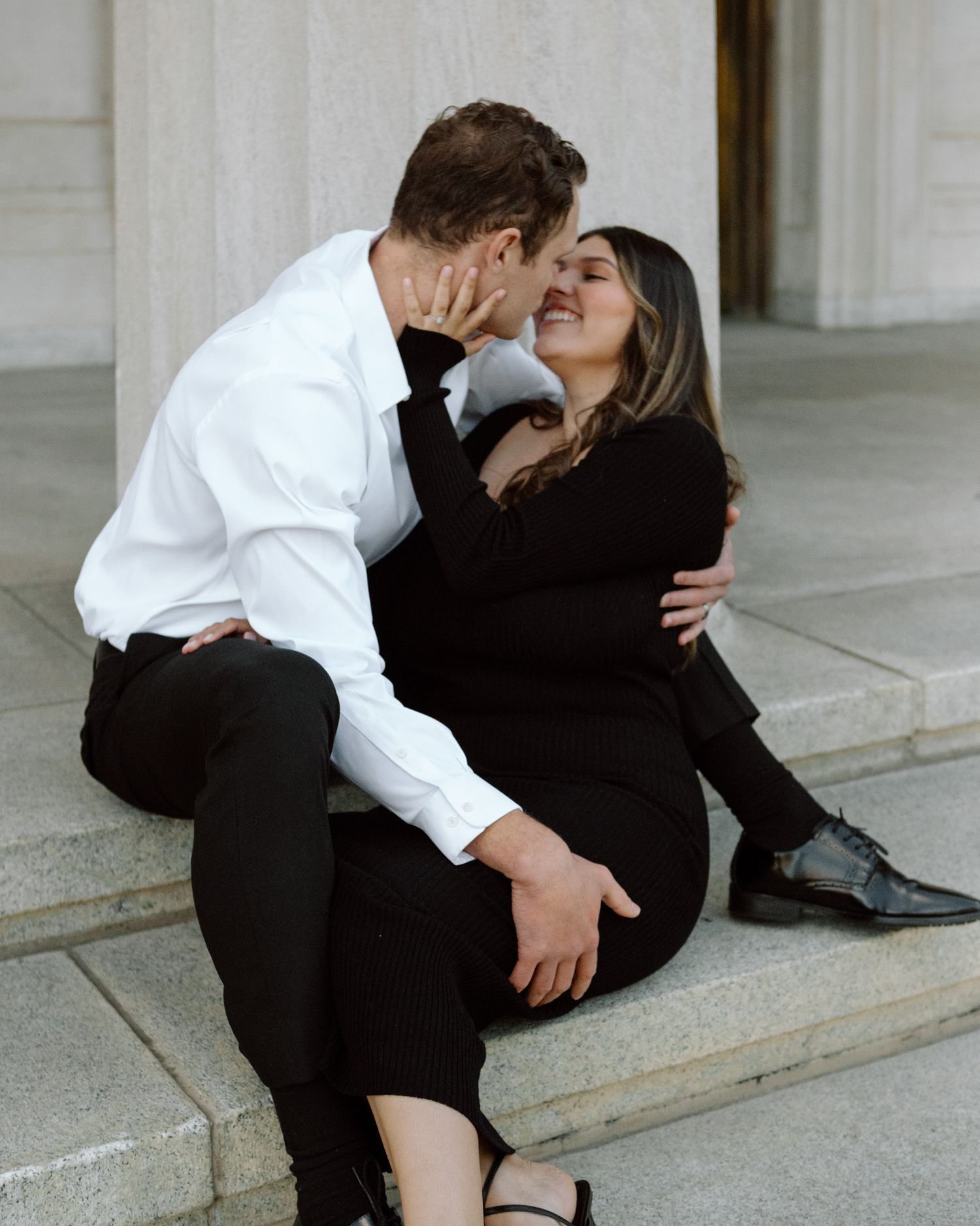 Engaged couple in downtown Louisville, with the woman smiling and showing her engagement ring while embracing her fiancé