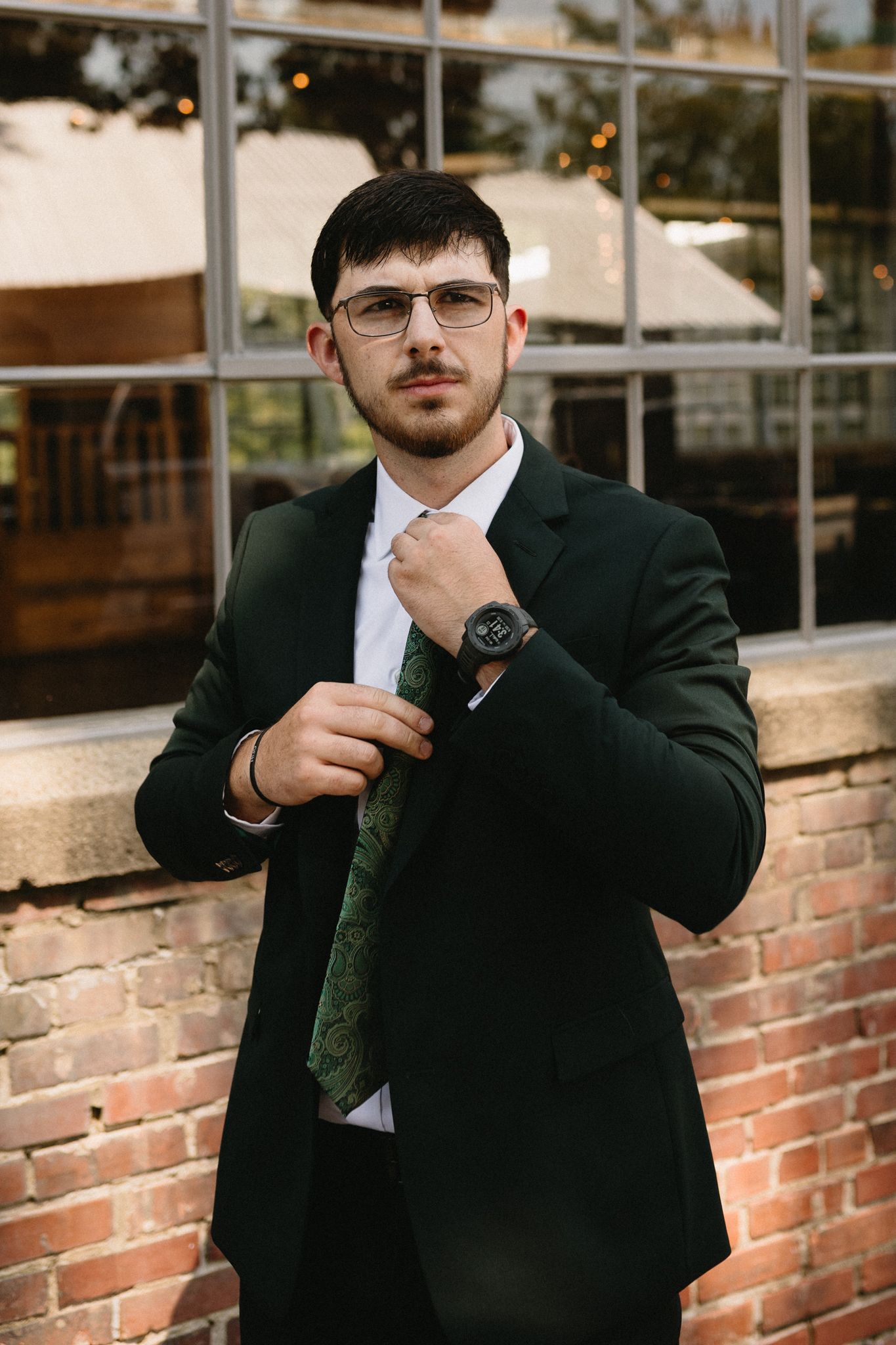 groom standing in front of brick wedding venue, getting ready and adjusting neck tie