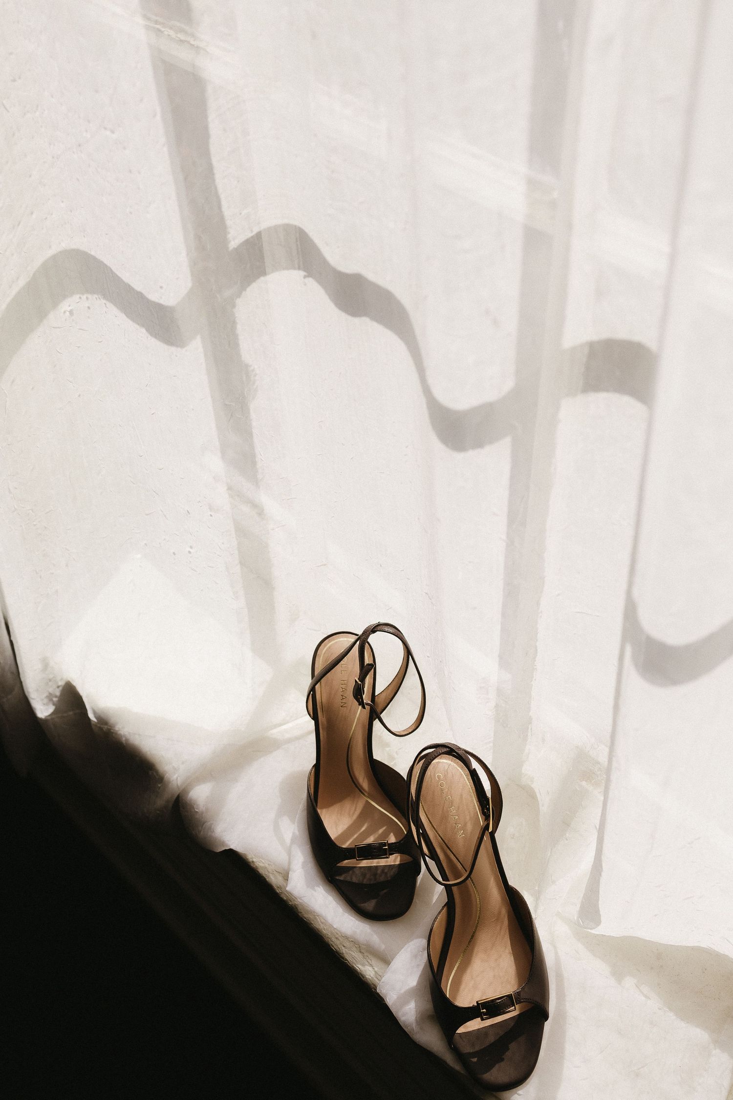 Artistic silhouette of black strappy wedding heels against white fabric.