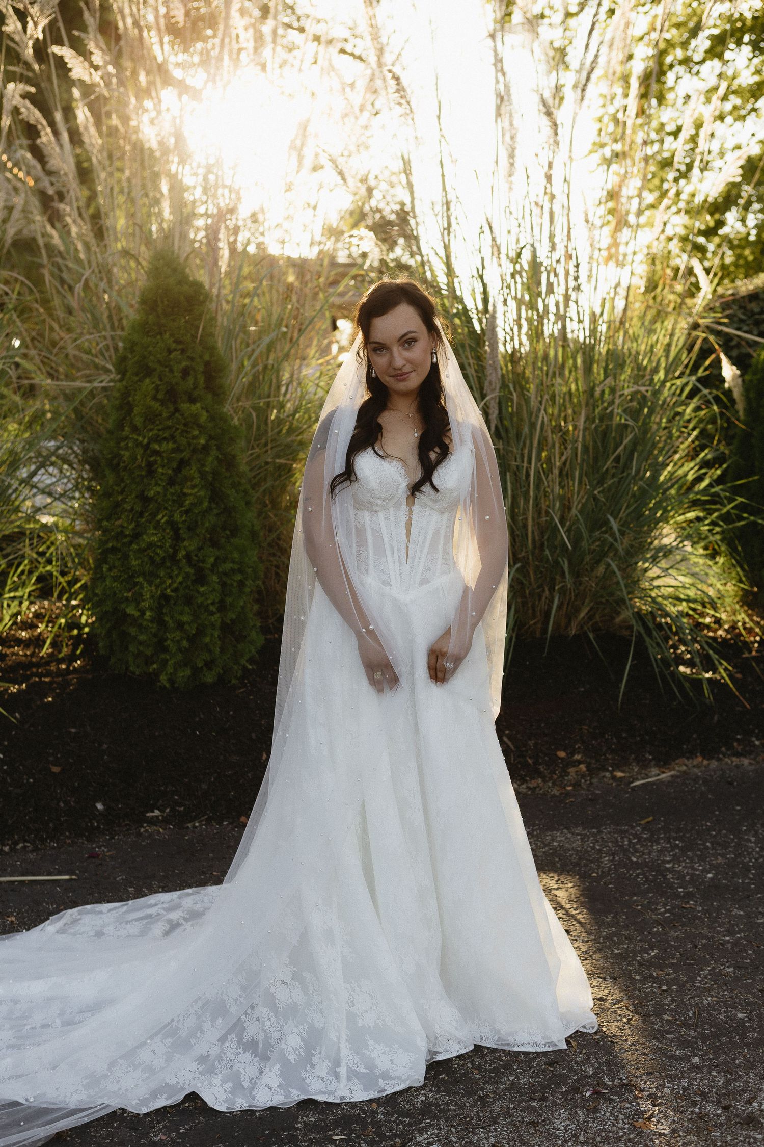 Bride's wedding dress flowing in backlit garden setting with tall grasses.