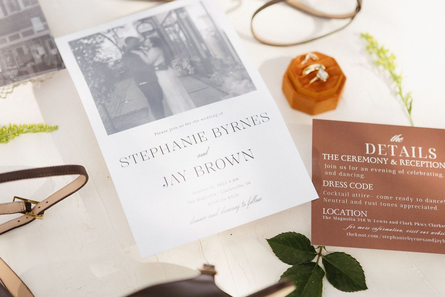 Wedding invitation suite with details card and black and white photo displayed with floral elements and amber glass decor.
