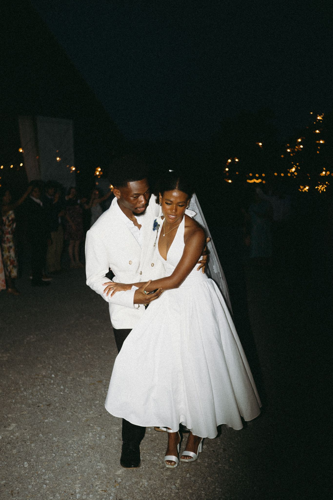 Wedding couple dances together under evening lights at an outdoor reception.