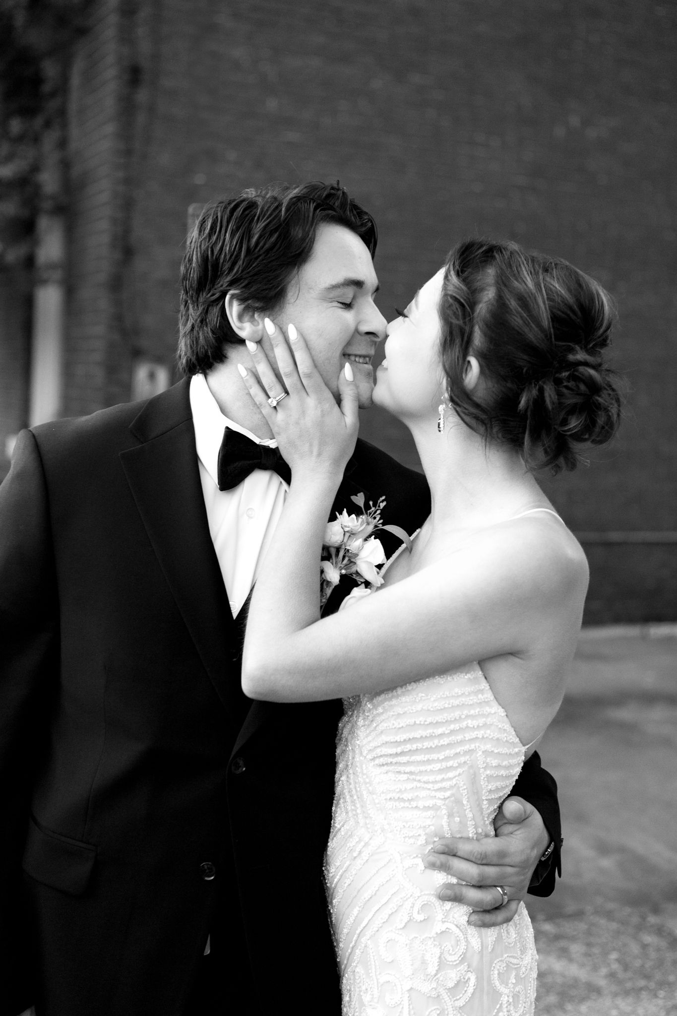 An intimate black and white wedding portrait with a couple in formal attire against a brick wall.
