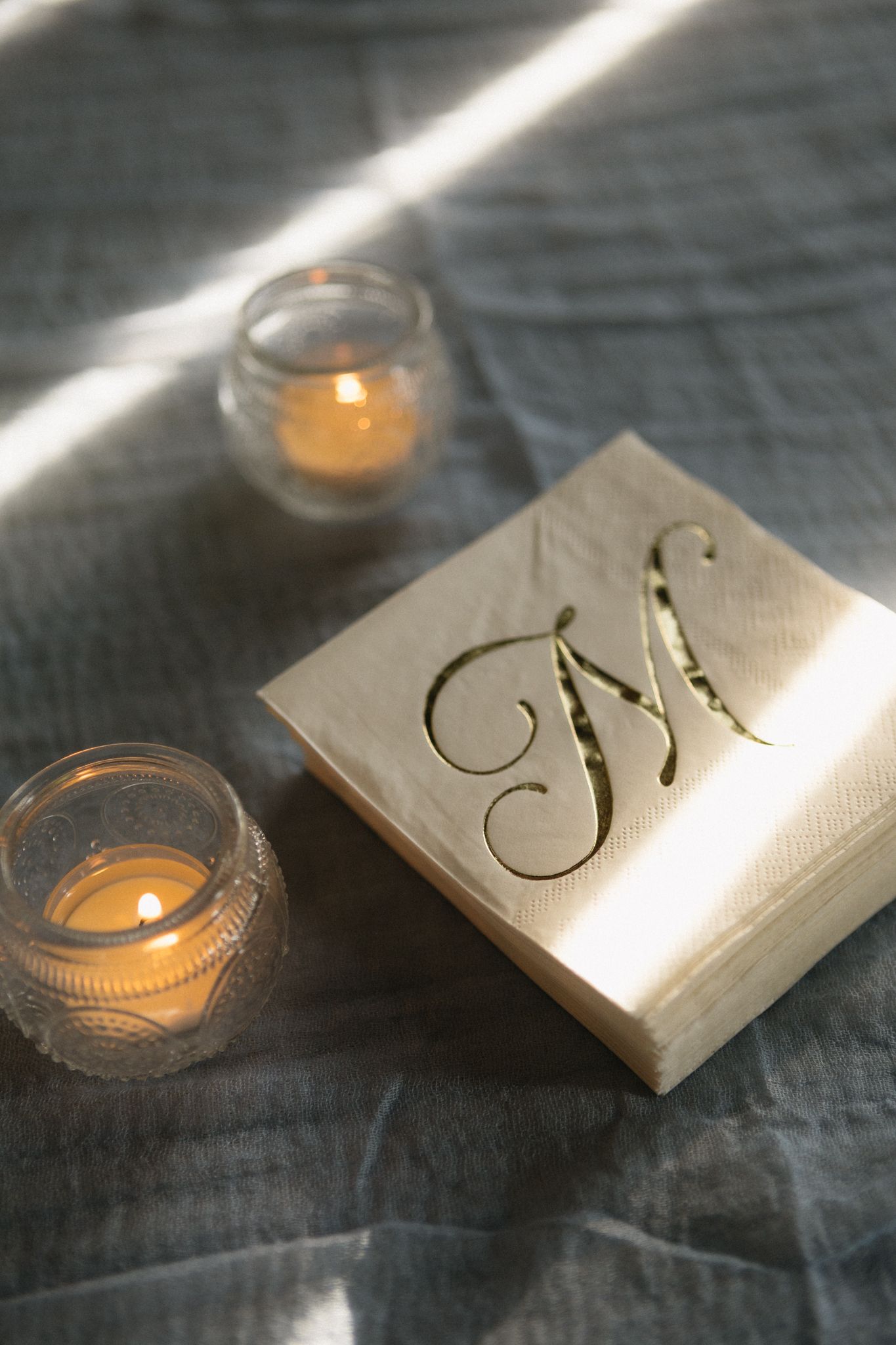 Wedding monogram displayed elegantly with glowing tea lights on dark textured fabric.