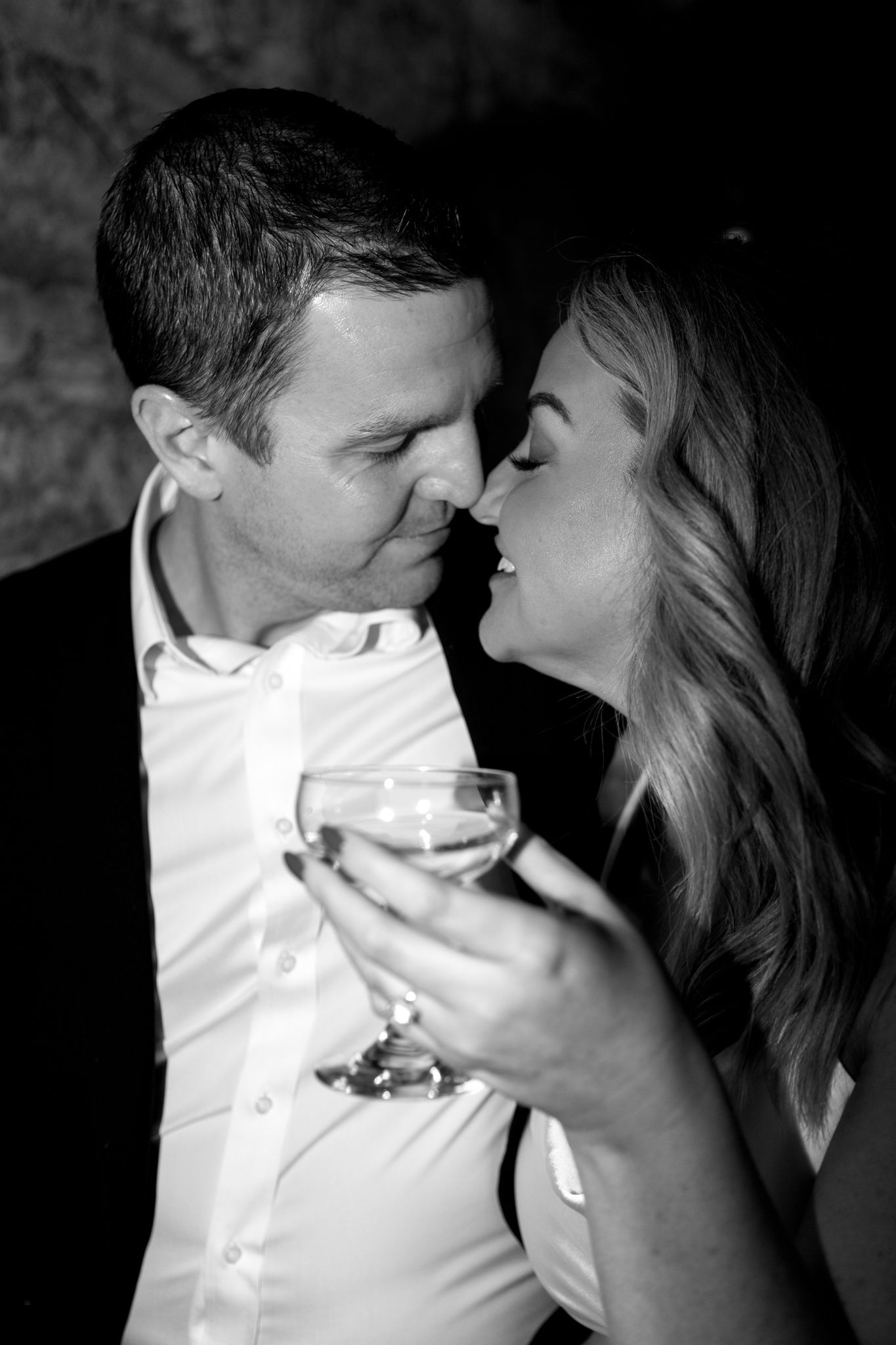 A black and white photo captures an intimate moment between a couple holding wine glasses.