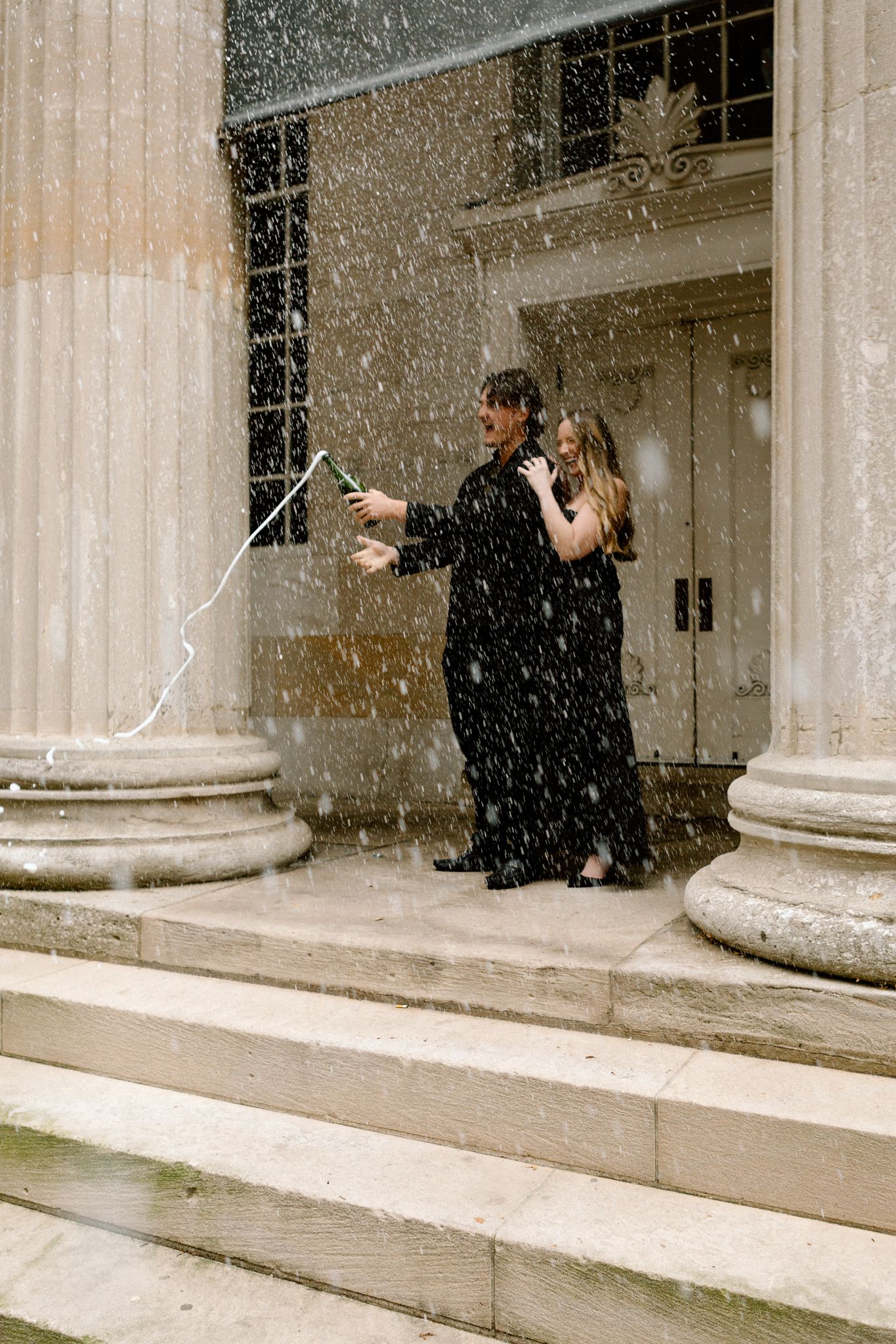 Engaged couple celebrating with a bottle of Chandon, sharing a joyful moment and laughter in downtown Louisville