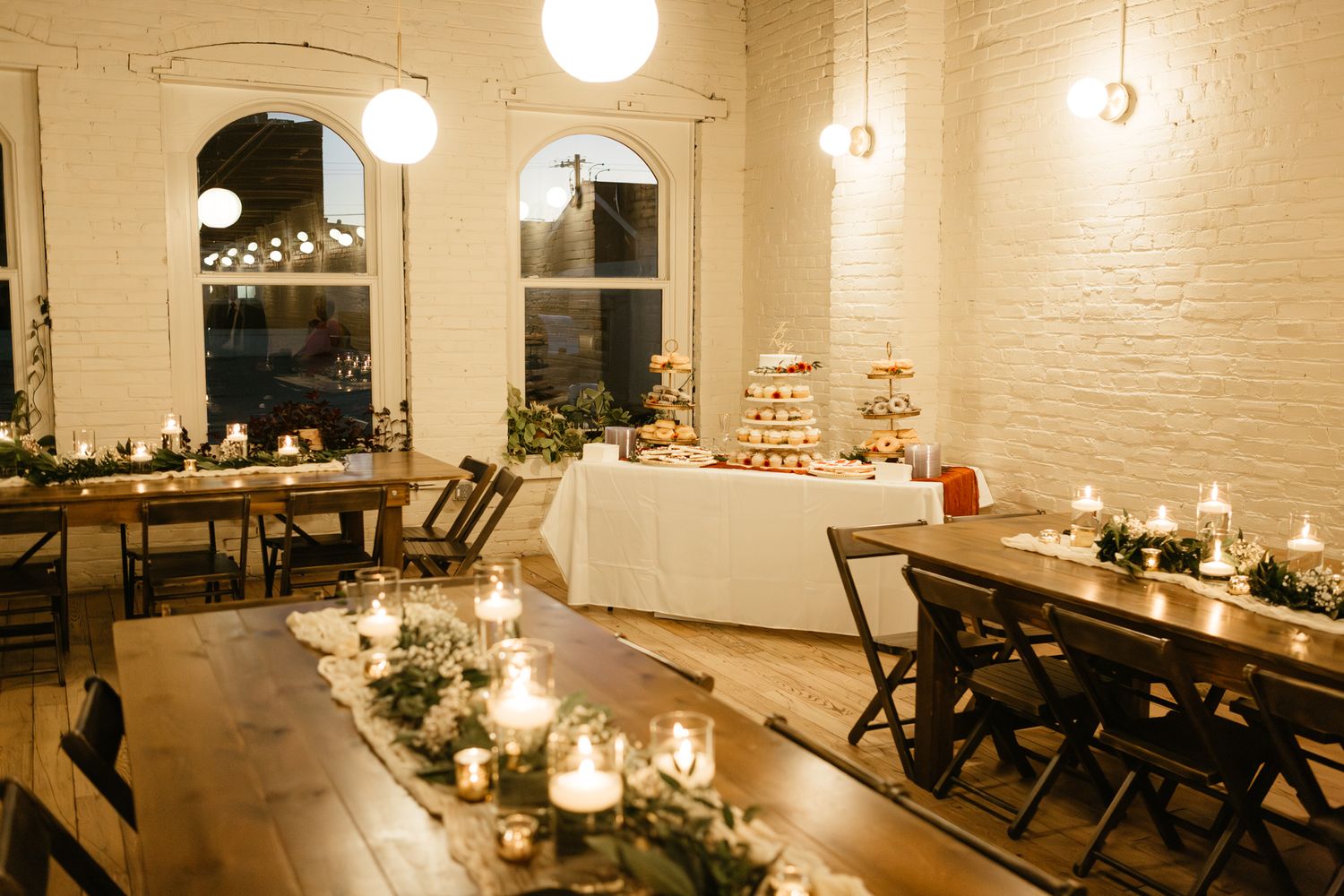 Elegant reception dining room with long tables, candlelight and white brick walls.