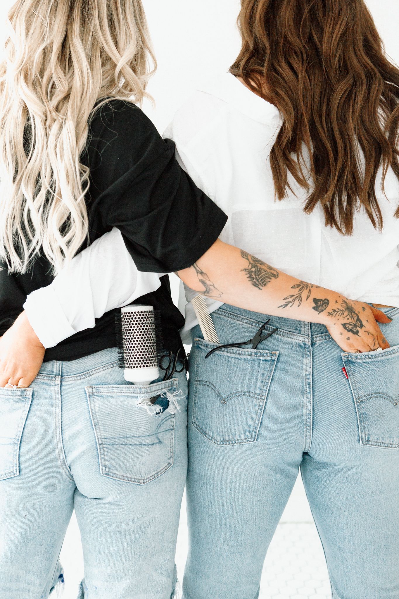 Two women in light wash Levi's jeans seen from behind, one with blonde hair and one with a tattooed arm.