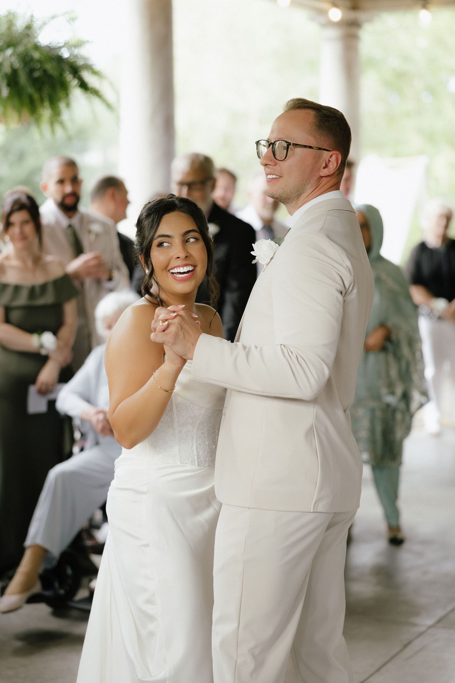 Bride in white strapless gown and groom in ivory suit share joyful first dance at wedding reception.