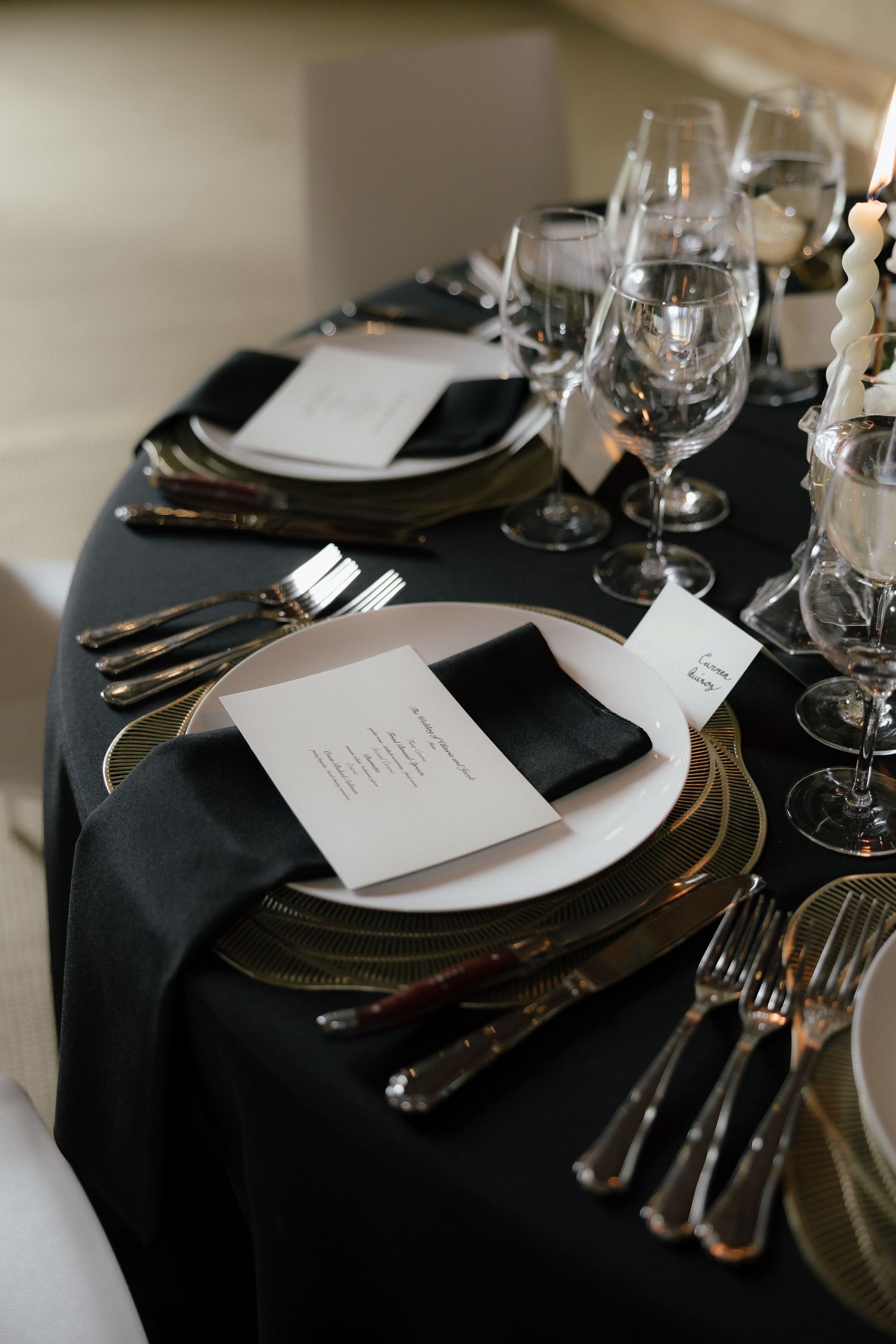 Elegant black and white wedding reception table setting with gold chargers and black linen napkins.