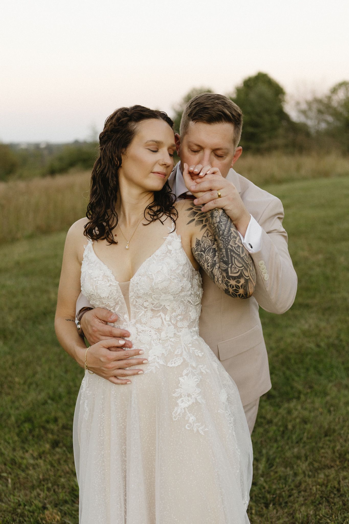 Romantic outdoor wedding couple embracing in a sunlit meadow during golden hour.