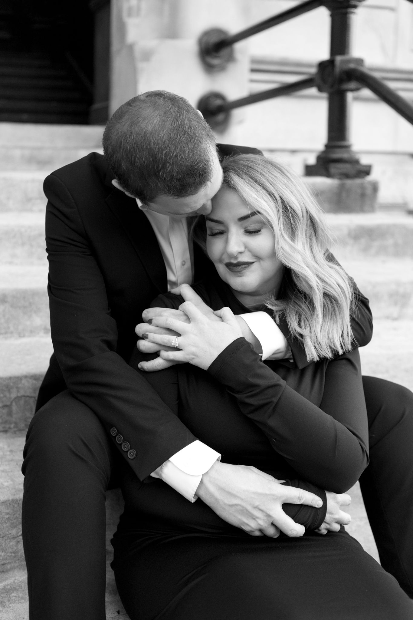 A romantic black and white portrait of a couple embracing on stone steps, showing tender affection.