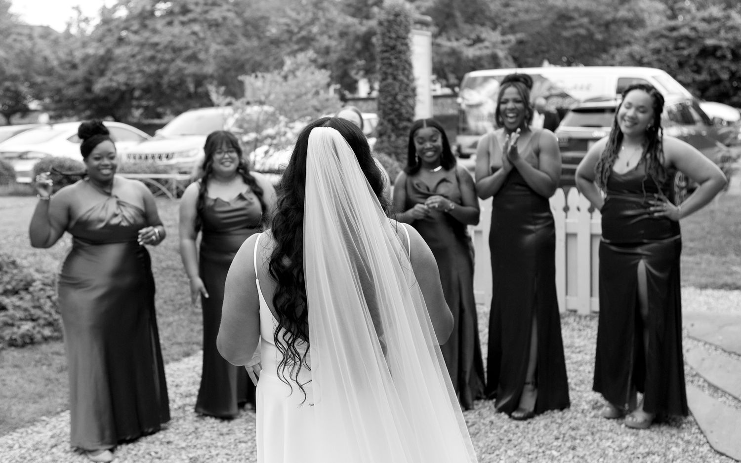 Black and white photo showing a wedding party celebrating together outdoors with joyful expressions and formal attire.