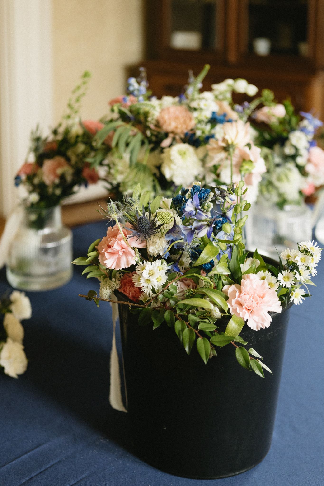 Black centerpiece containers filled with pink and blue flowers with greenery arranged on navy blue tablecloths.