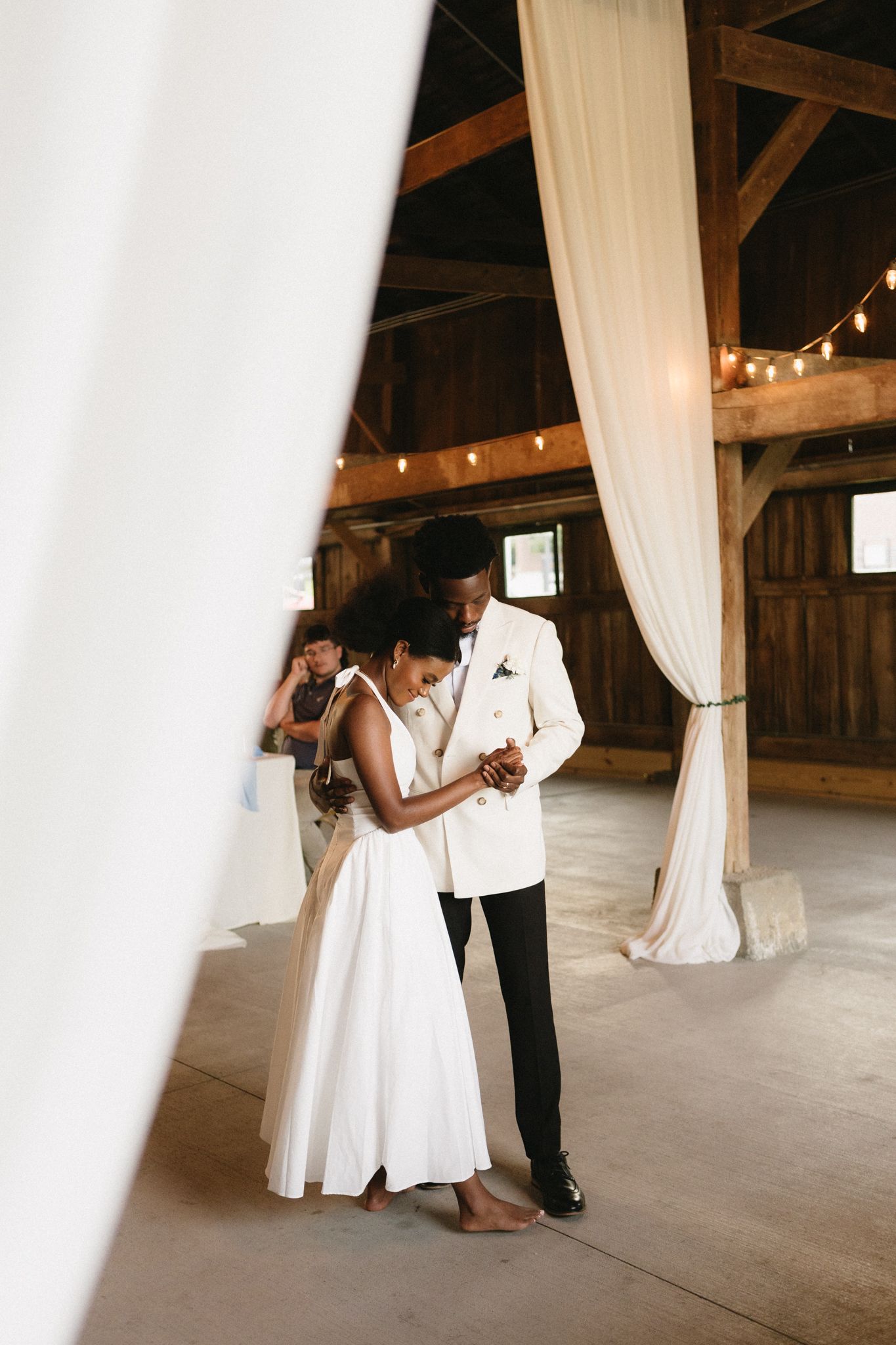 Romantic dance sequence in rustic barn venue with flowing white drapes and string lights.