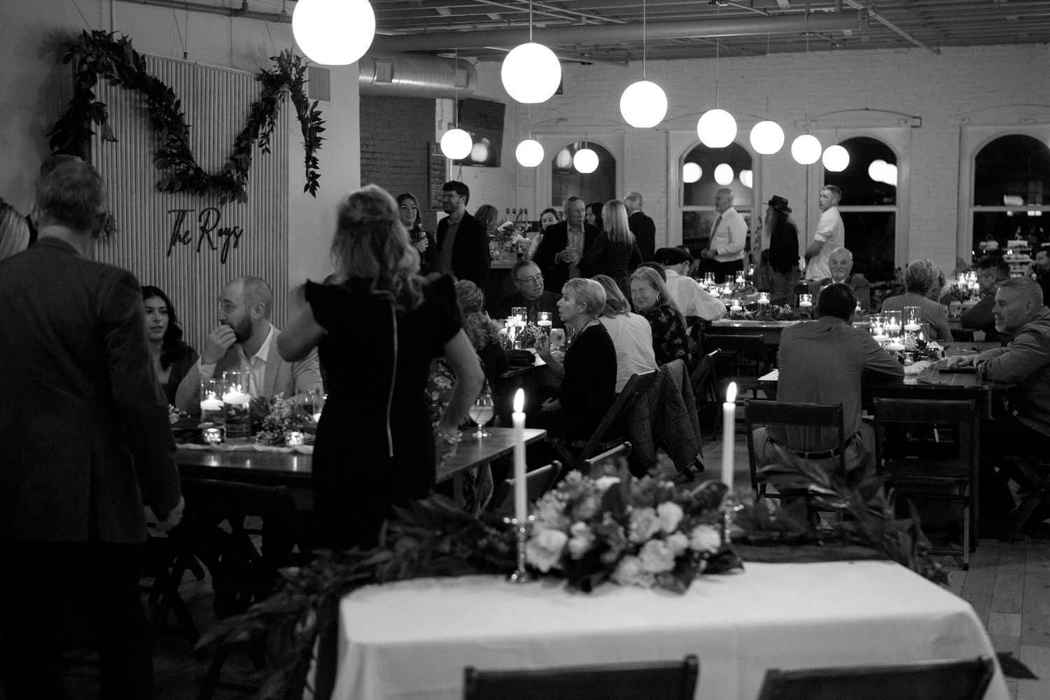 Black and white photo of an event space with paper lanterns, candlelit tables, and floral centerpieces.