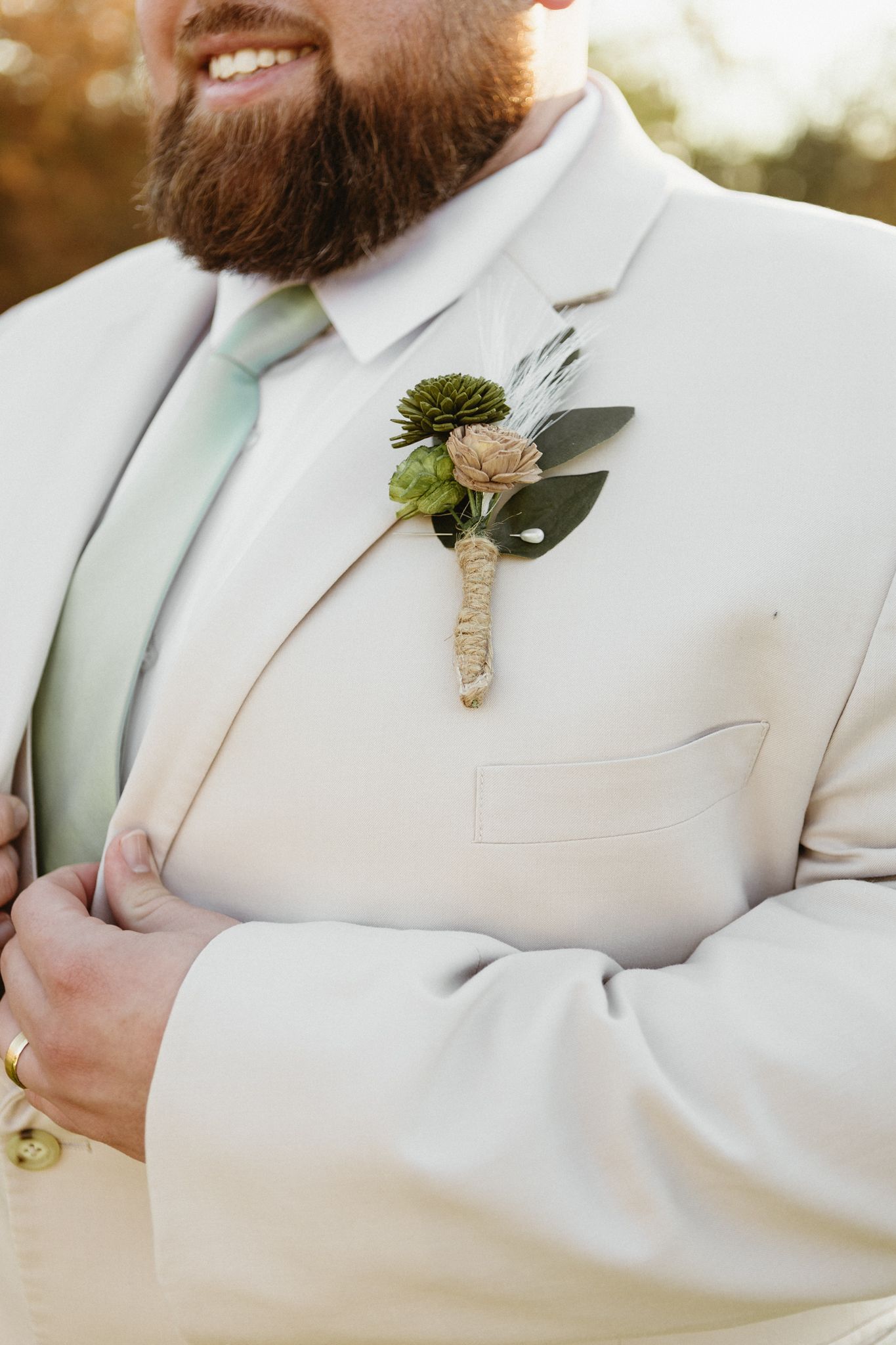 Close-up details of a cream suit jacket with mint tie and floral boutonniere.