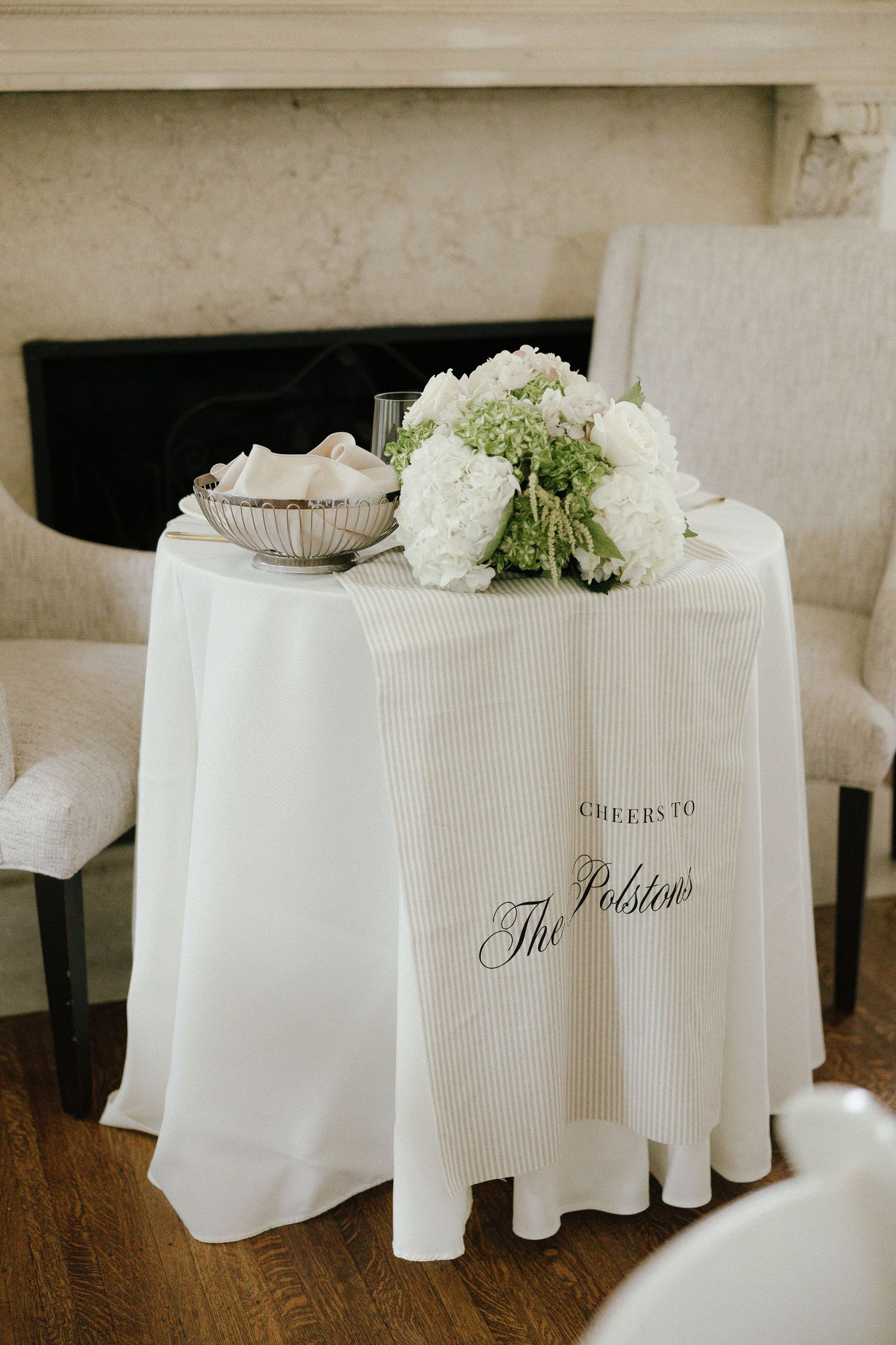 Elegant sweetheart table with white linen reads Cheers to The Polsteins with white floral centerpiece.
