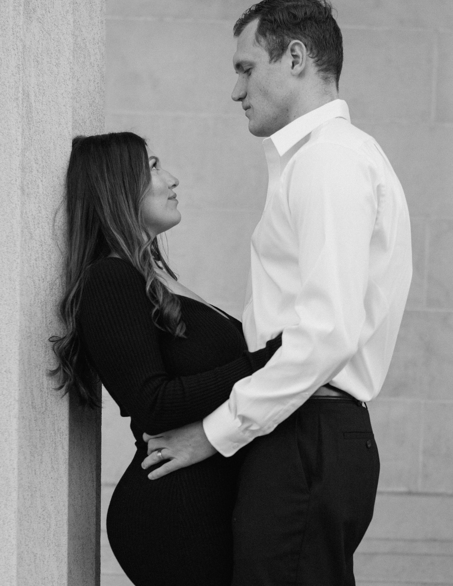 Engaged couple in downtown Louisville, with the woman smiling and showing her engagement ring while embracing her fiancé