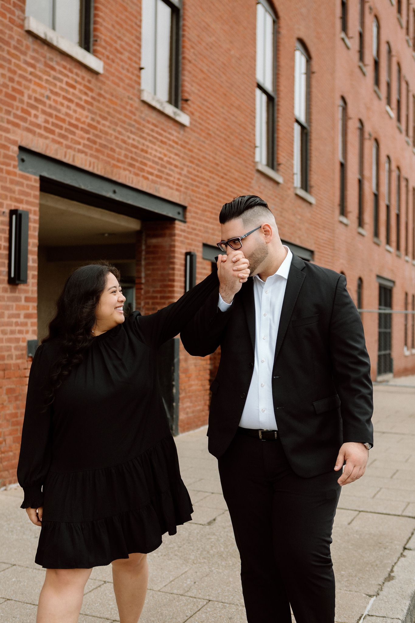 Elegant engaged couple smiling and embracing in downtown Louisville, with the woman showing her engagement ring