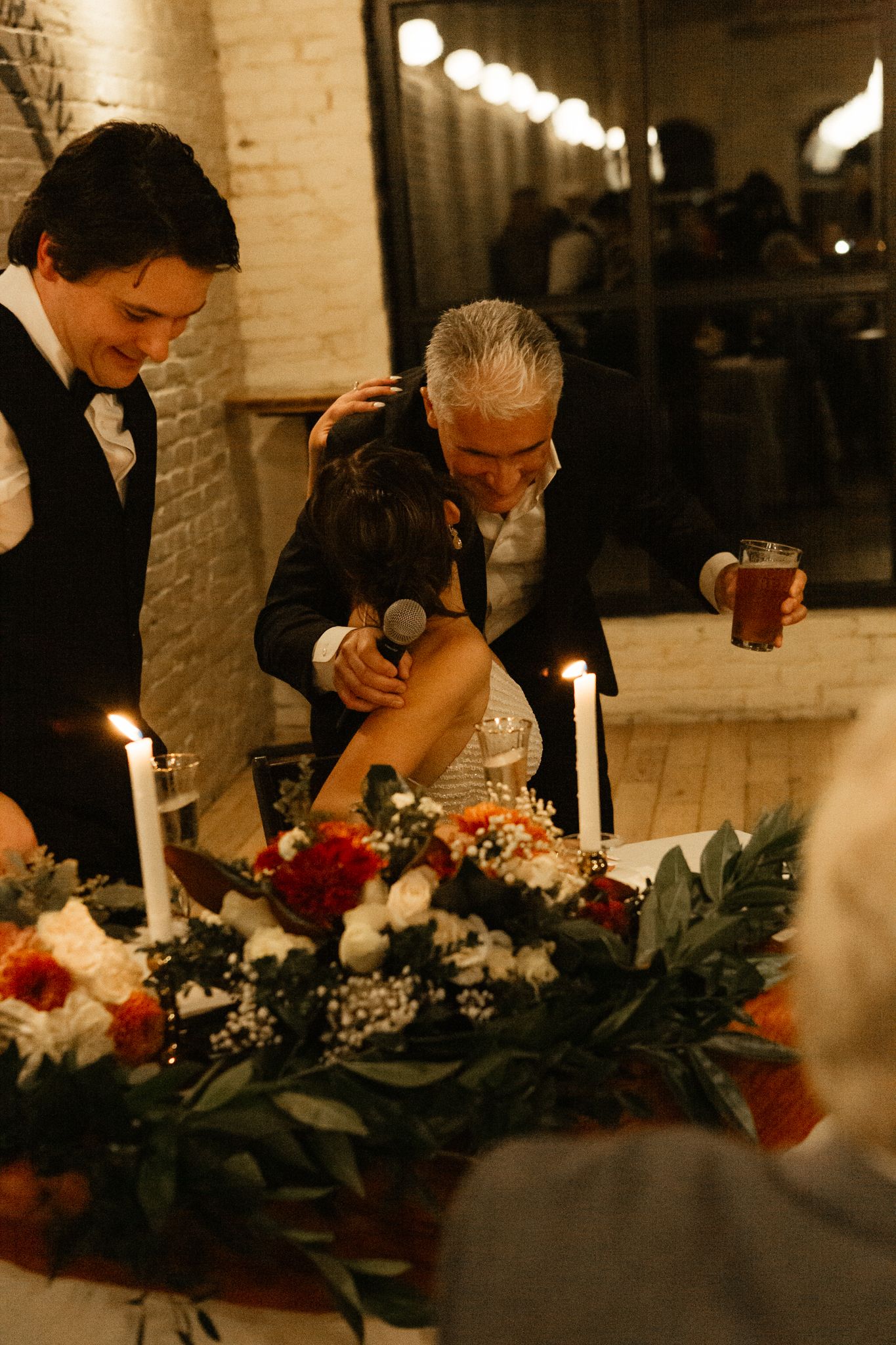 People gathering around an elegant table with candles and floral arrangements at a wedding celebration.