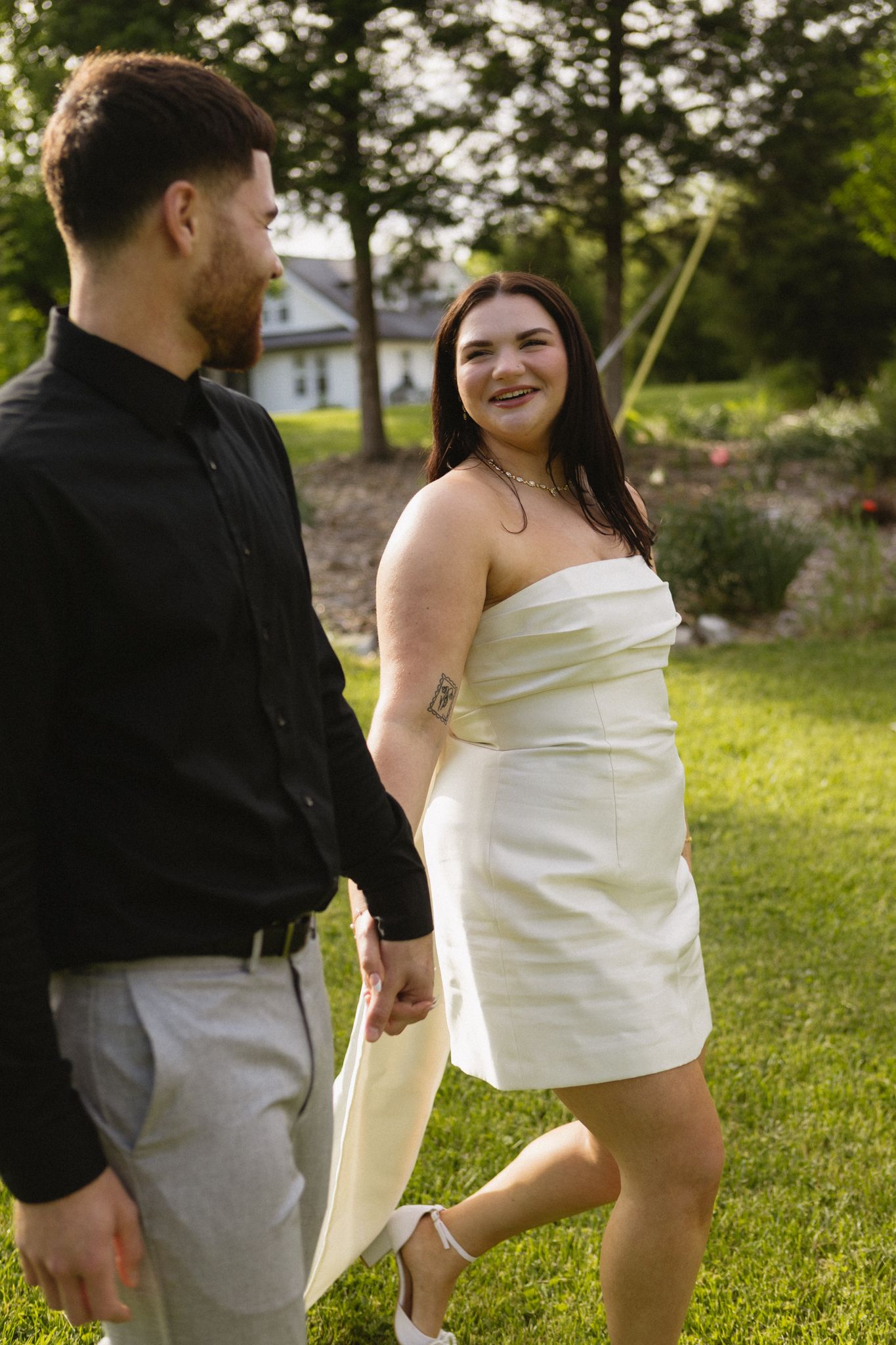 A couple in wedding attire stands together on a grassy lawn during their special day.