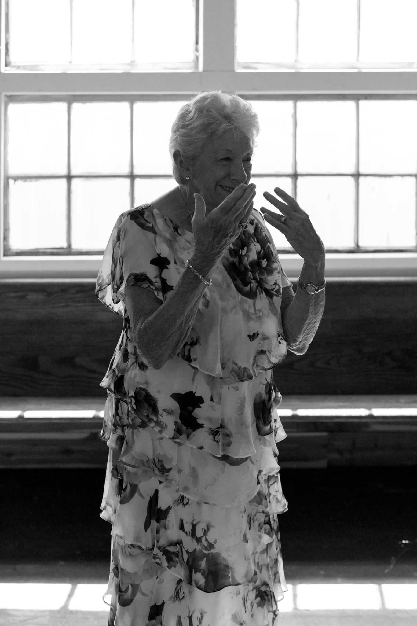 An older woman joyfully laughs, standing by a window, radiating warmth and happiness in a bright, inviting space
