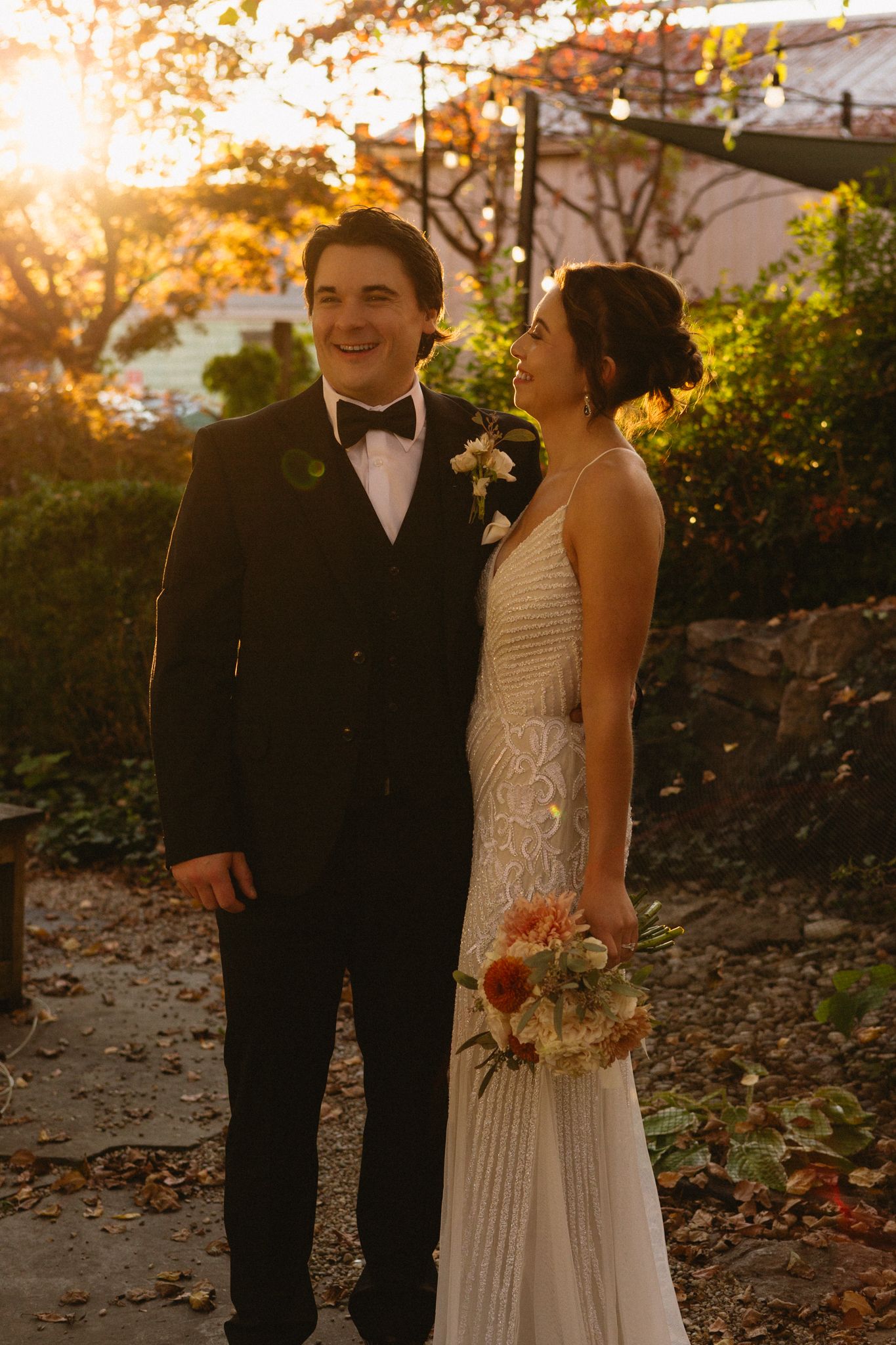 Sunset wedding portrait of couple in formal attire against autumn foliage.