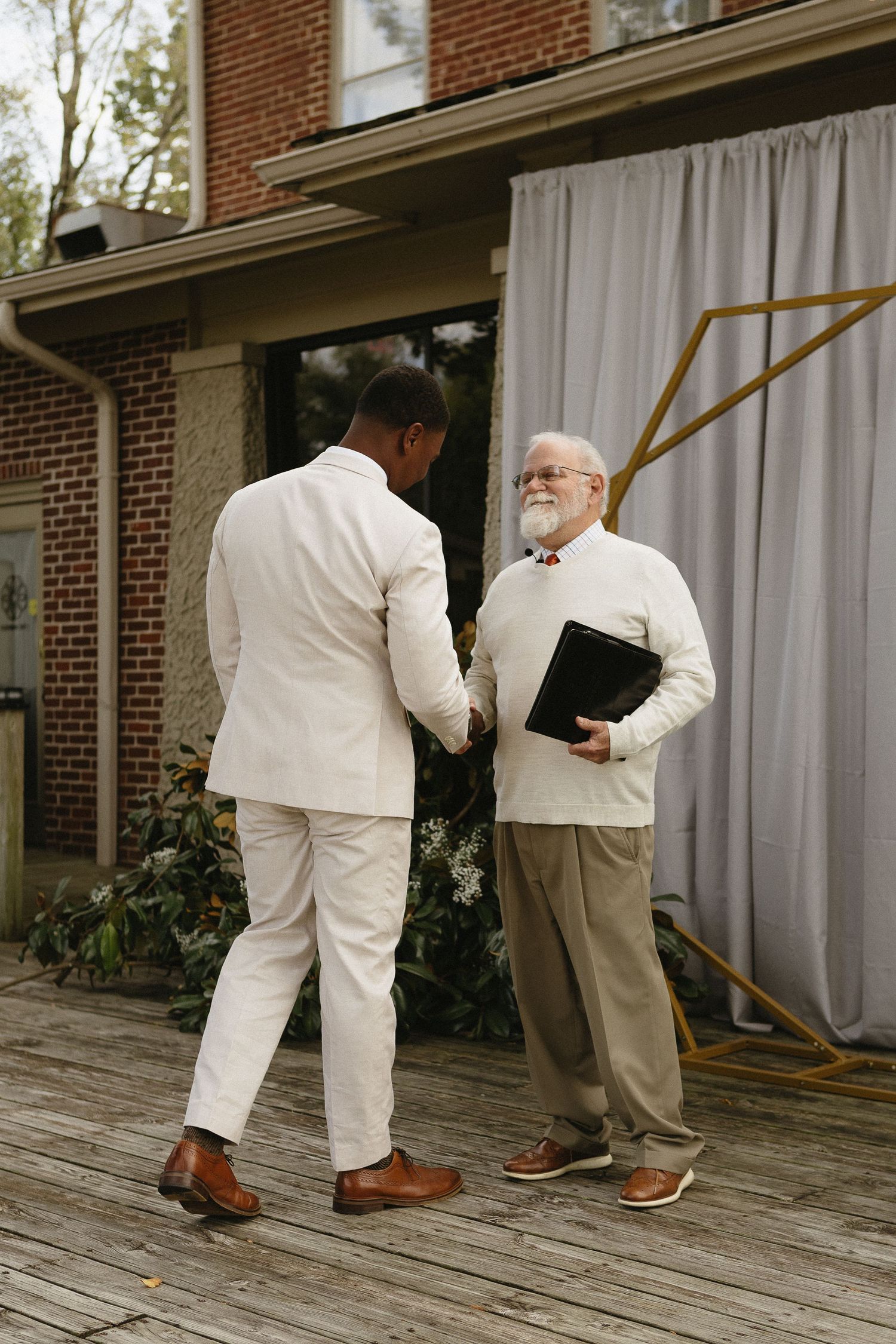 Wedding party members in white suits adjust their attire on an outdoor deck.