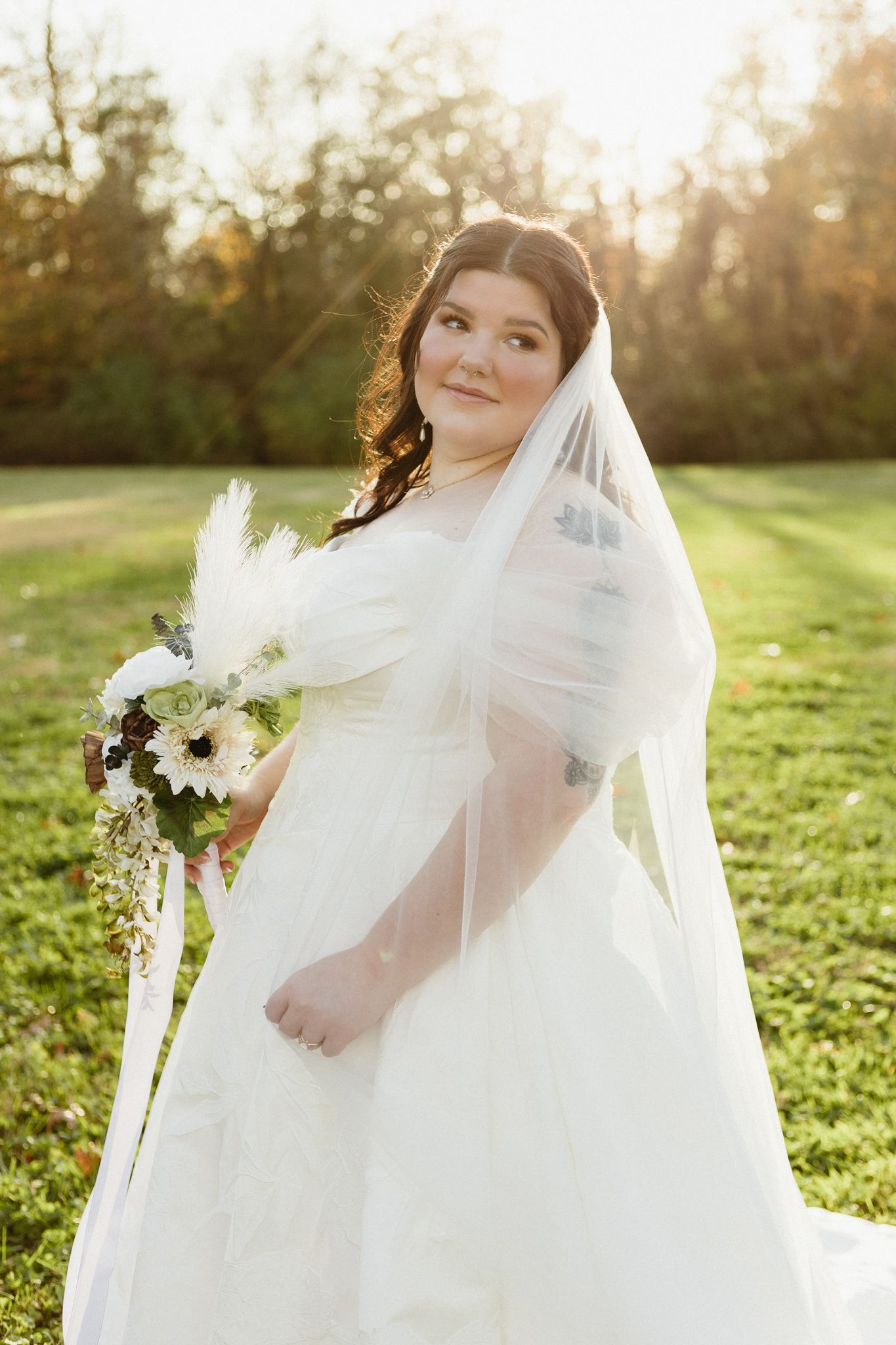 Sunlit bridal portraits in a grassy field with flowing white wedding dress and veil during golden hour.