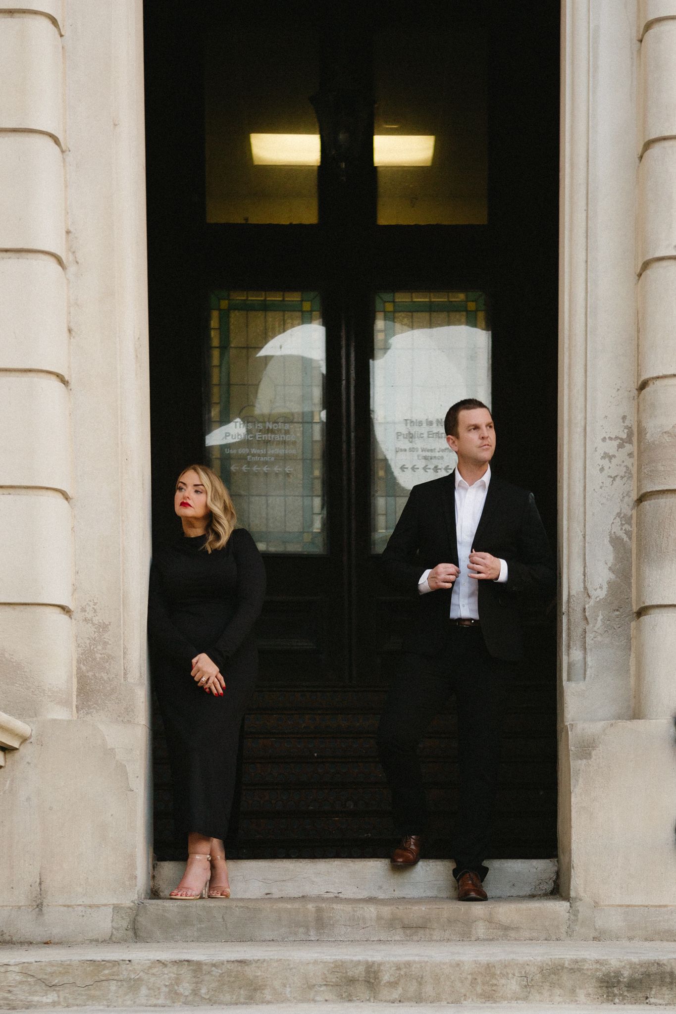 Couple in formal wear standing separately in a doorway for a stylish portrait.