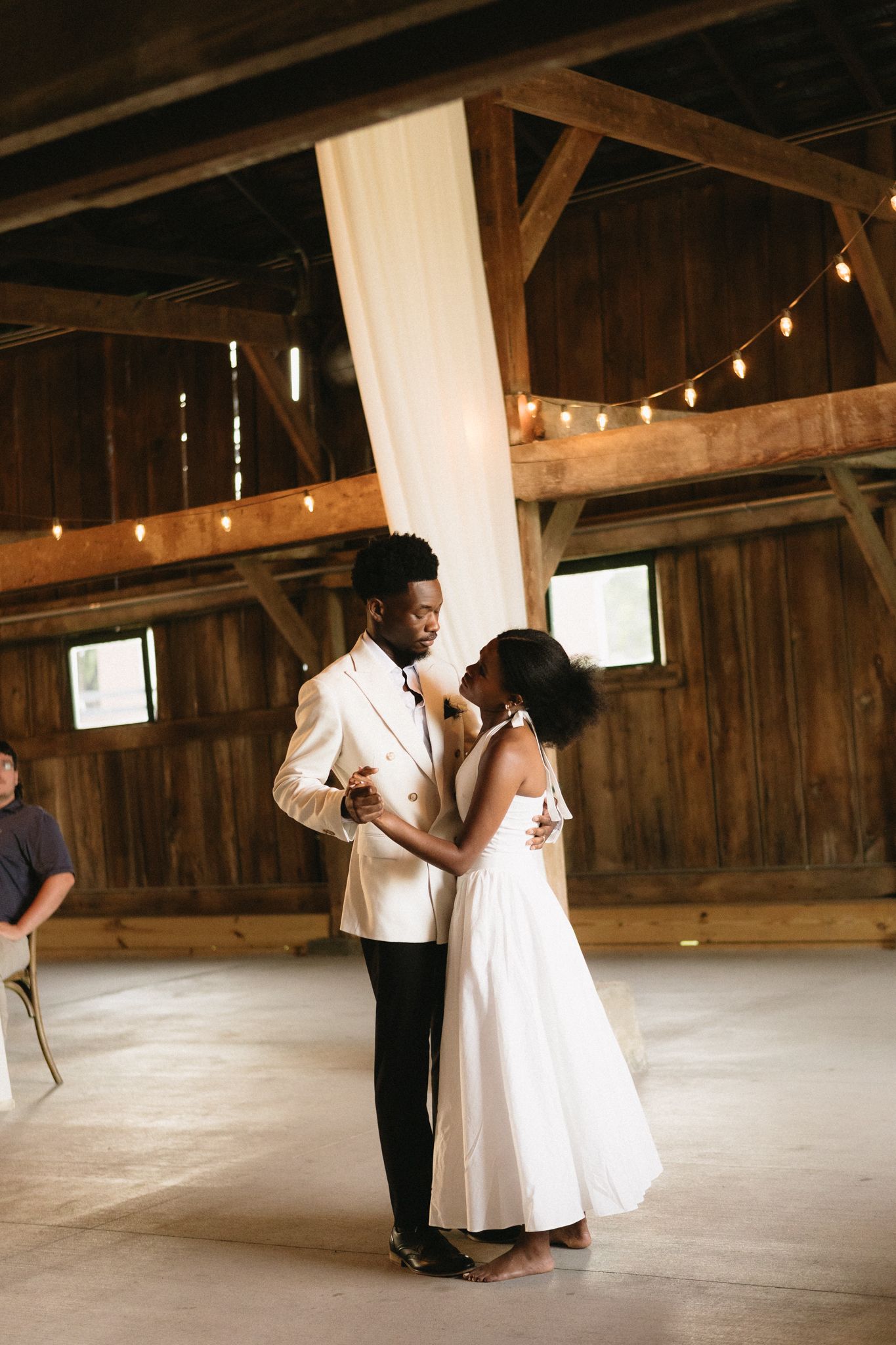 A romantic moment during a first dance in a rustic barn venue decorated with string lights.
